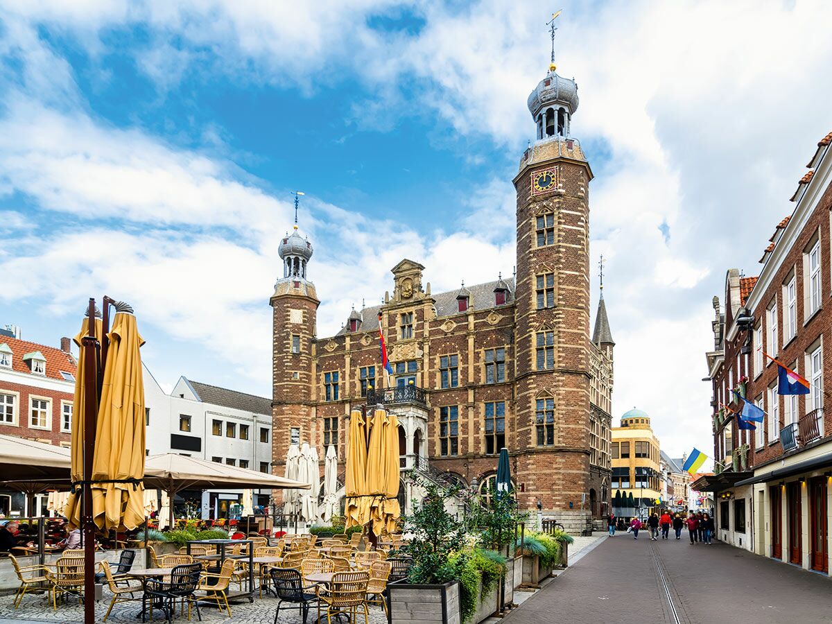 Historisches Rathaus in Gouda, Niederlande, am belebten Marktplatz mit Außengastronomie und Passanten bei Tag.