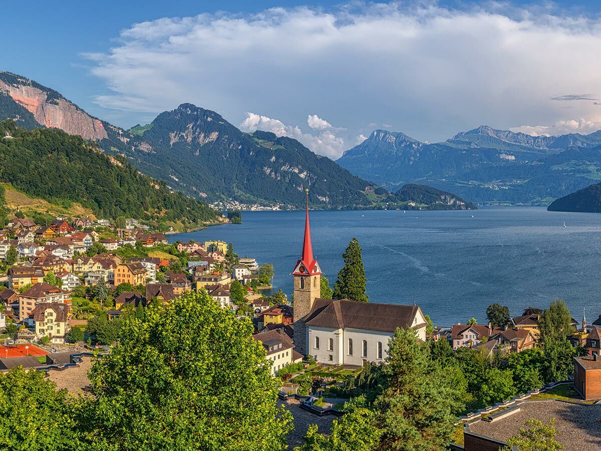 Malerische Schweizer Stadt am Ufer eines blauen Alpensees mit roten Kirchtürmen und bewaldeten Bergen unter blauem Himmel.
