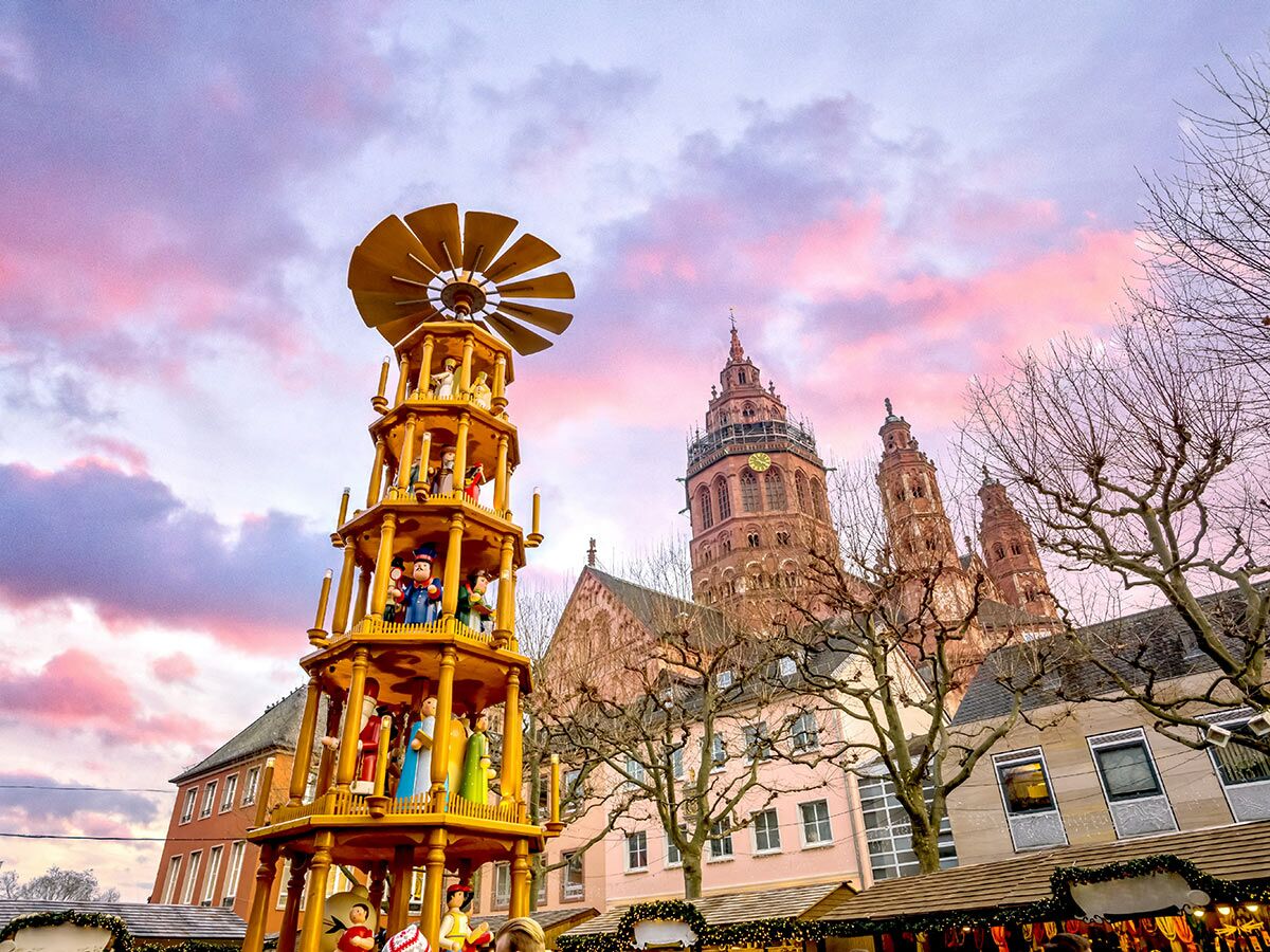 Große Holz-Weihnachtspyramide auf dem Mainzer Weihnachtsmarkt vor der beleuchteten Kathedrale unter rosa-lila Abendhimmel.