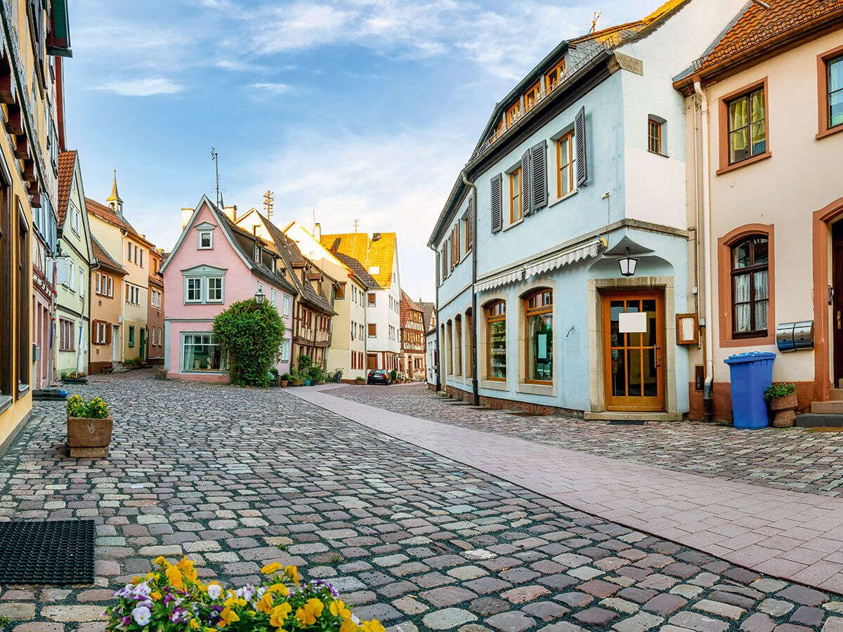 Malerische Altstadtgasse mit traditionellen, farbigen Häusern, Kopfsteinpflaster und Blumen an einem sonnigen Tag.