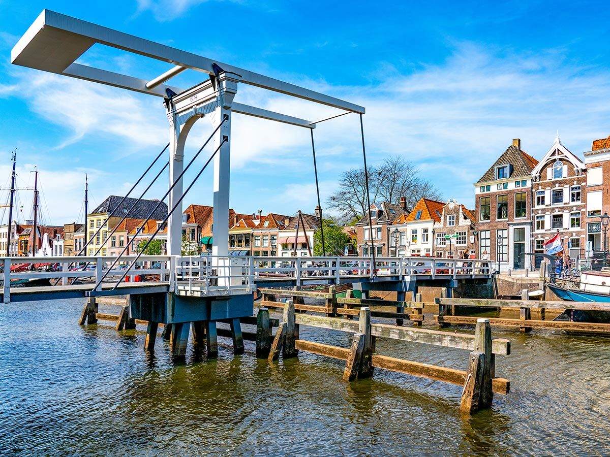 Weiße Zugbrücke über einer Gracht in einer niederländischen Stadt mit bunten historischen Häusern unter blauem Himmel.