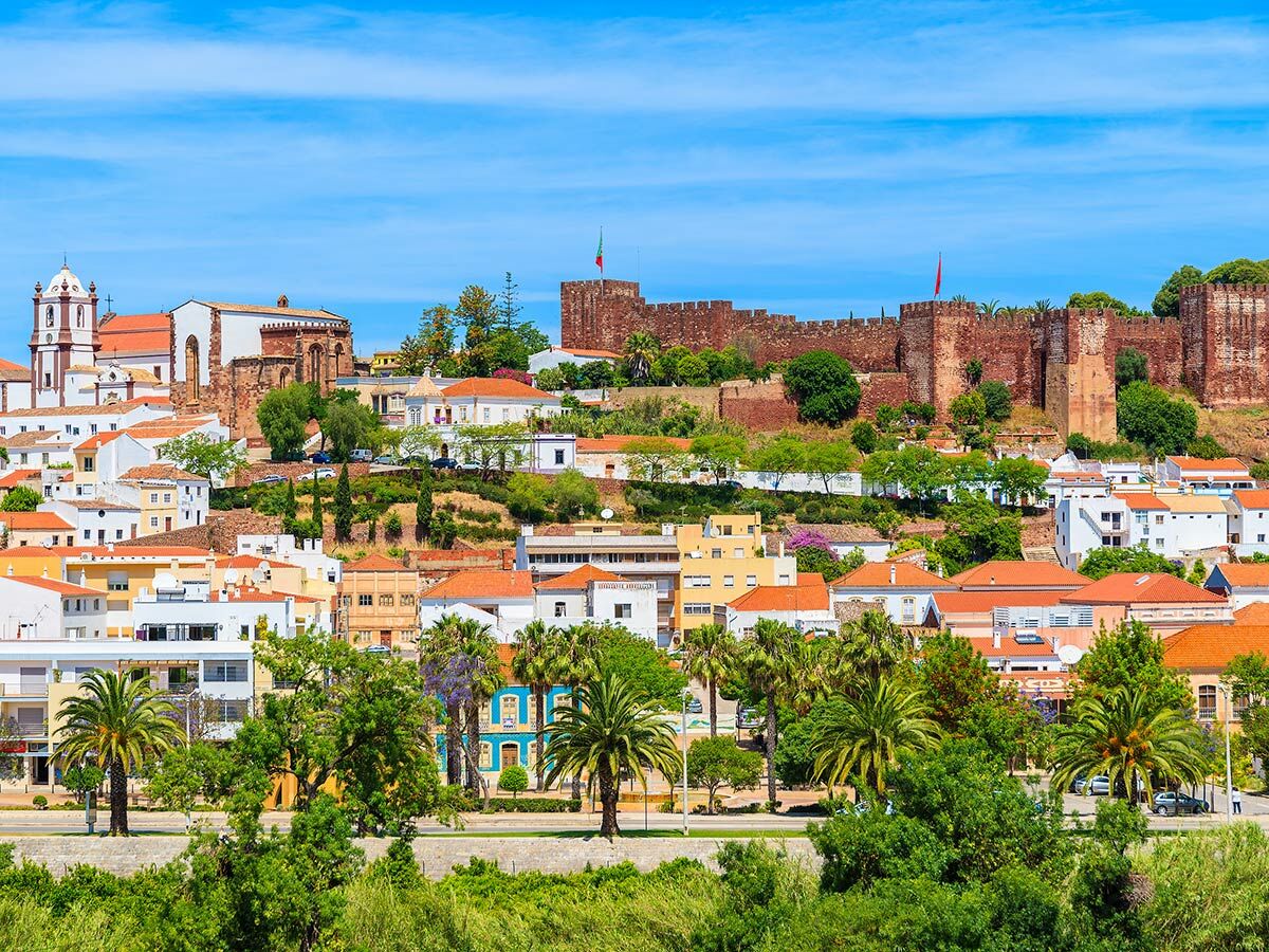 Panoramablick auf Silves, Portugal, mit der historischen Burg und Kathedrale über einer Stadt mit Palmen.
