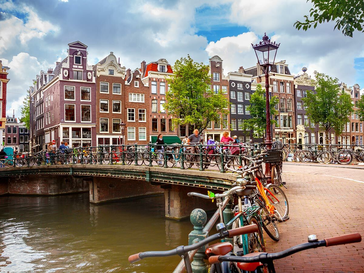 Lebhafte Szene in Amsterdam mit Gracht, Brücke voller Fahrräder und Menschen, umgeben von historischen Giebelhäusern unter blauem Himmel.