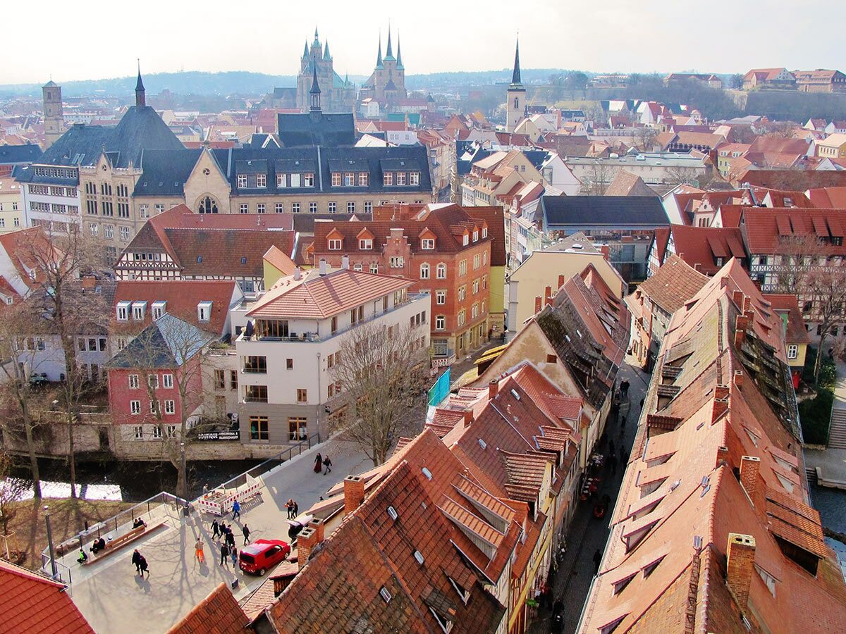 Luftaufnahme der historischen Altstadt von Erfurt mit roten Dächern, engen Gassen, einem Fluss und der Kathedrale im Hintergrund.