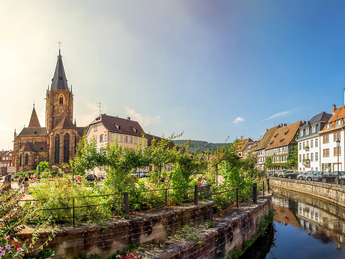 Malerische europäische Altstadt mit großer Kirche, traditionellen Gebäuden und einem ruhigen Kanal unter blauem Himmel.