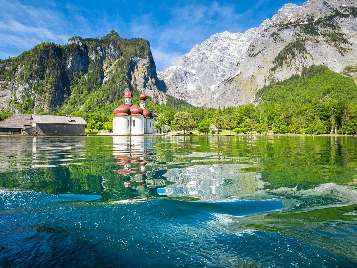 Ikonische St. Bartholomä Kirche am Königssee mit roten Zwiebeltürmen, umgeben von grünen Wäldern und dem Watzmann.