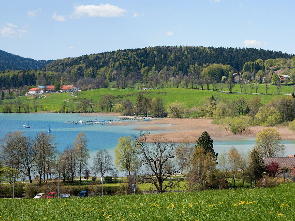 Panoramablick auf blauen See mit Segelbooten, grünen Wiesen, Wald und Häusern im Frühling in den Bergen.