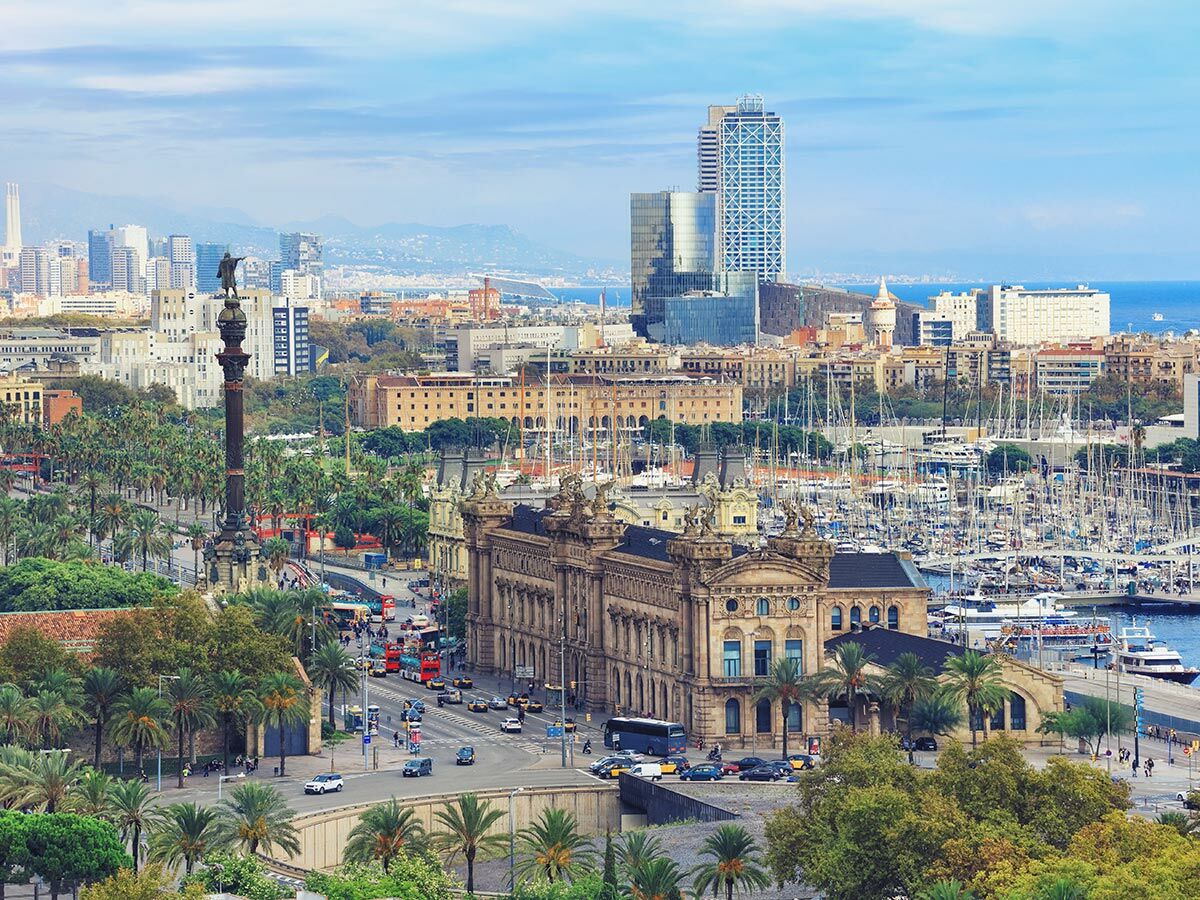 Panoramaaufnahme von Barcelona mit dem Columbus-Denkmal, geschäftigen Straßen, dem Hafen Port Vell voller Yachten und der Skyline am Meer.