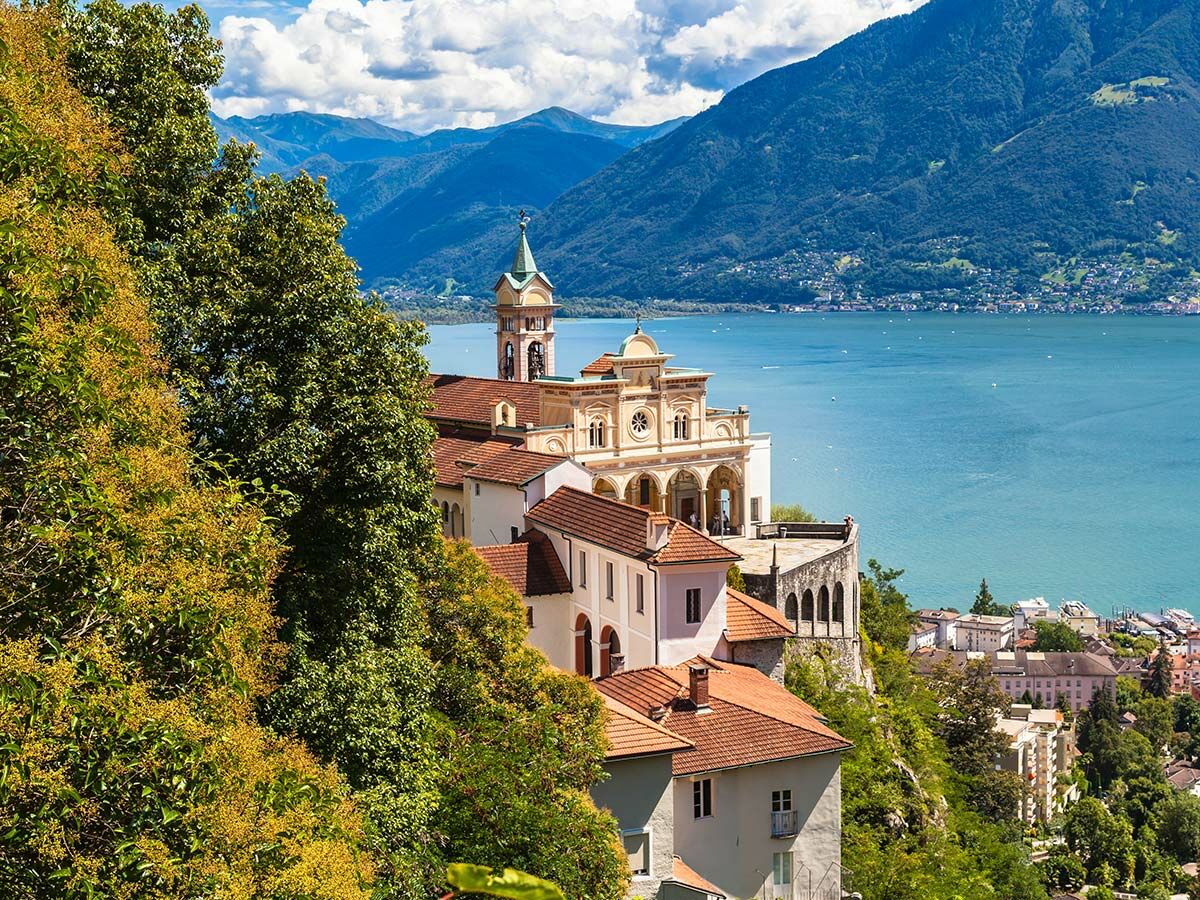 Panoramablick auf die Wallfahrtskirche Madonna del Sasso in Locarno über dem Lago Maggiore mit Bergen und blauem Himmel.