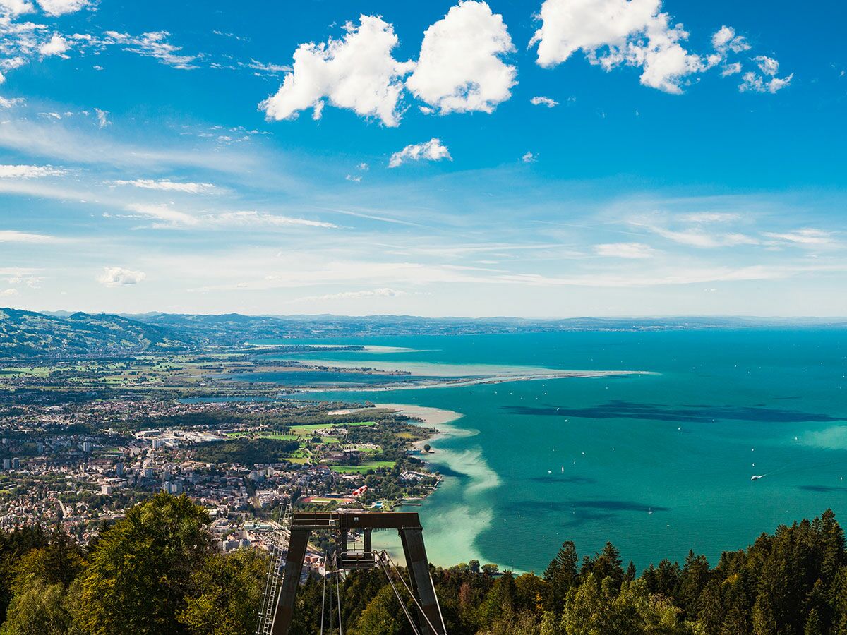Panoramablick auf den Bodensee, die Stadt Bregenz und die Alpen vom Pfänder mit blauem Himmel und weißen Wolken.