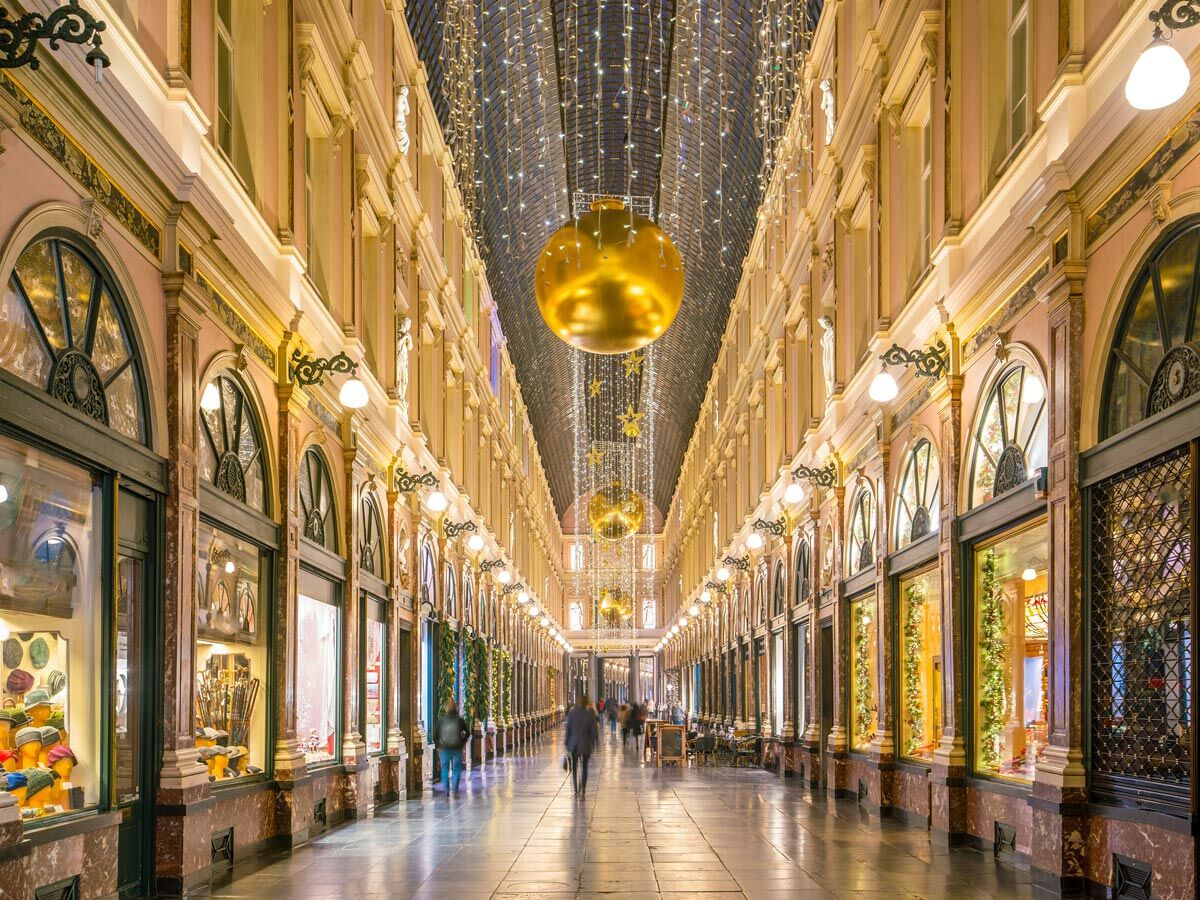 Elegante Einkaufspassage mit gläserner Decke, goldener Weihnachtsdekoration und beleuchteten Schaufenstern in der Abenddämmerung.