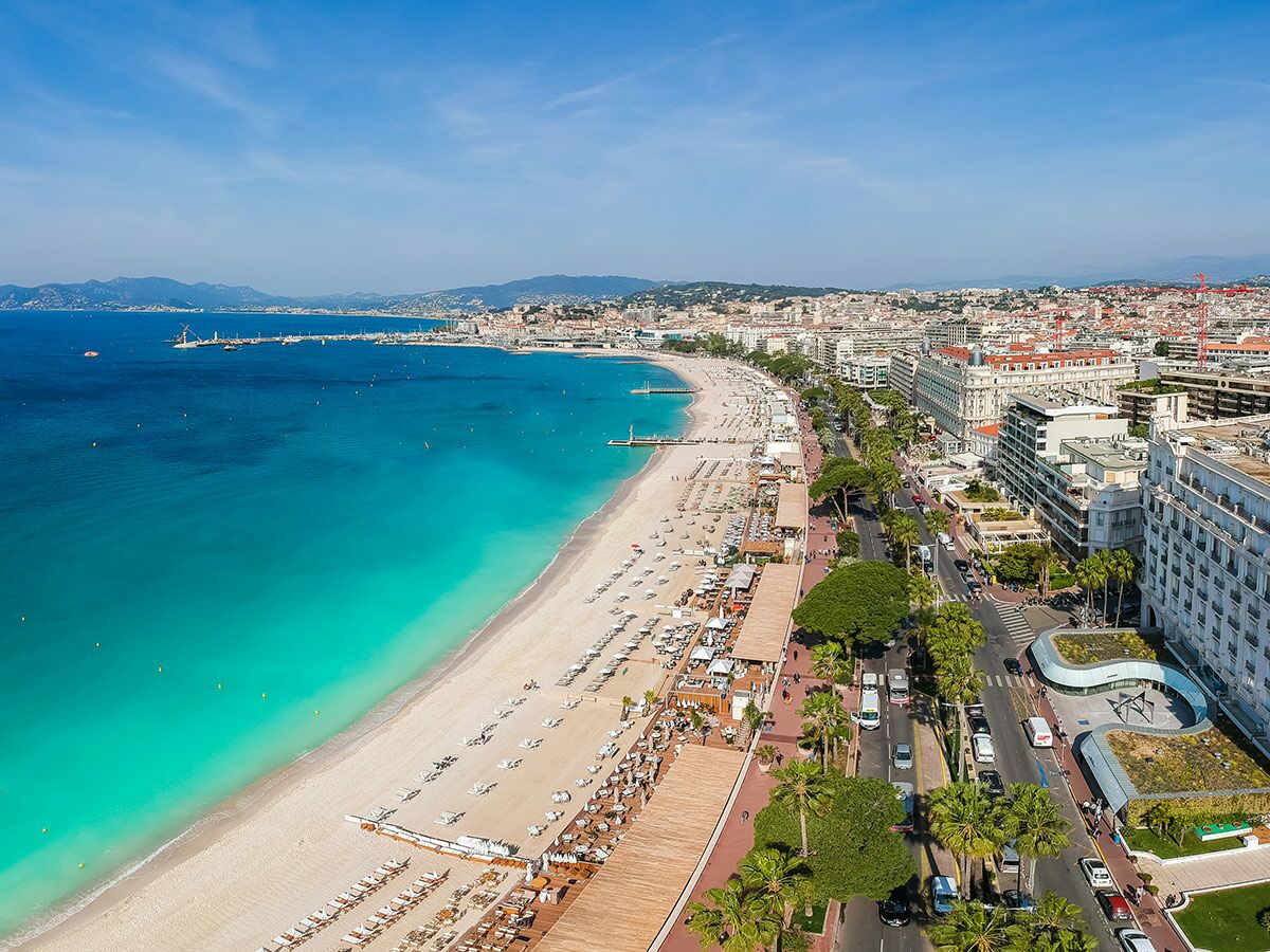 Luftaufnahme von Cannes mit langem Sandstrand, türkisfarbenem Meer, belebter Croisette und Stadtkulisse.