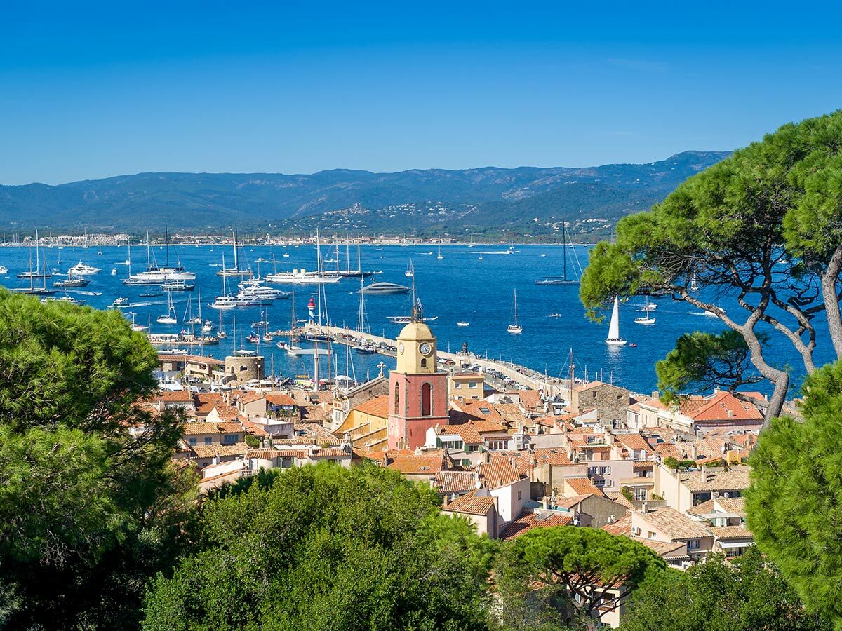 Panoramablick auf den sonnigen Hafen von Saint-Tropez mit luxuriösen Yachten, rot gedeckten Häusern und Kirchturm.