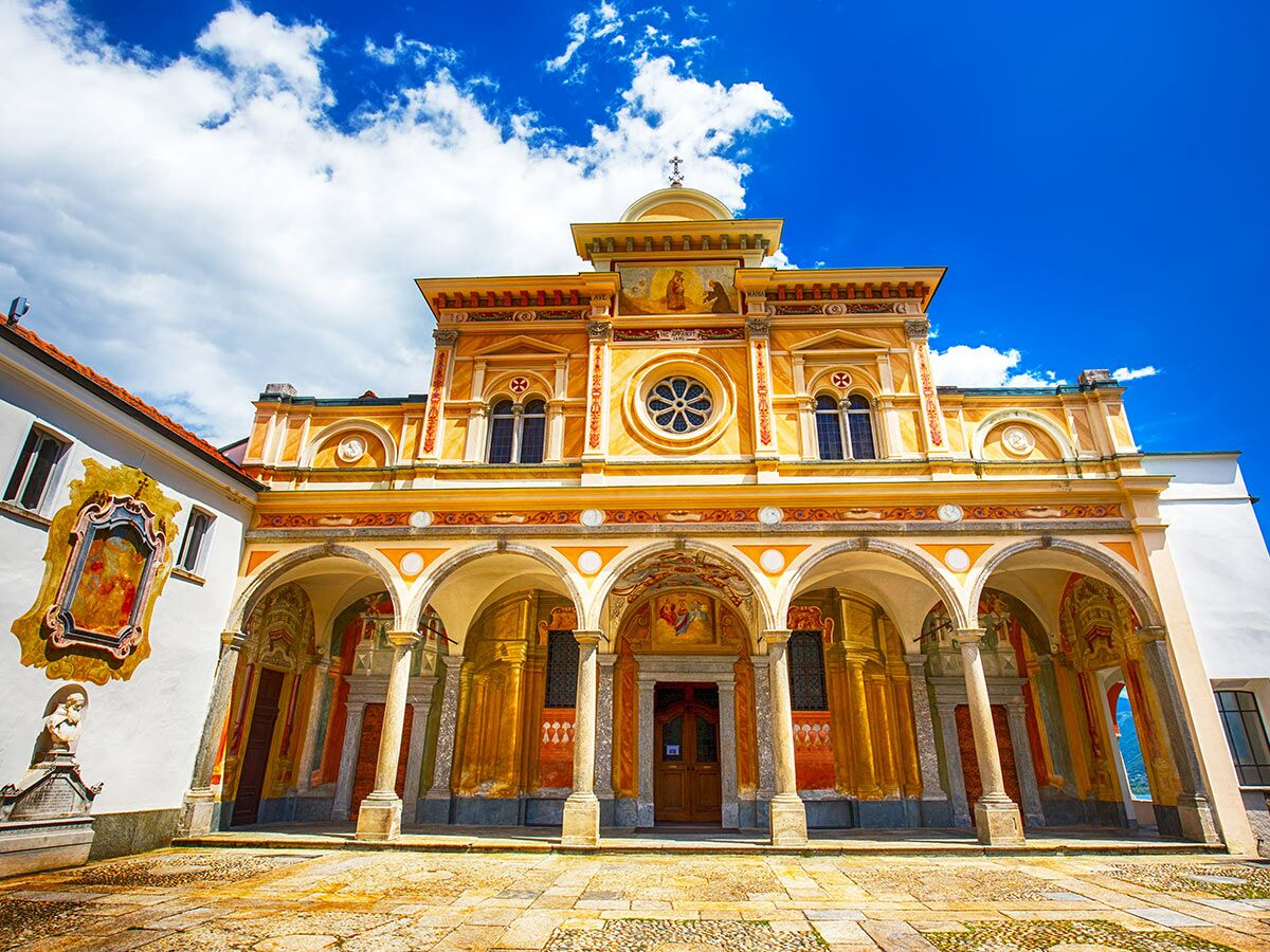 Historische italienische Kirche mit gelber Fassade, kunstvollen Fresken unter Arkaden und blauem Himmel mit Wolken.