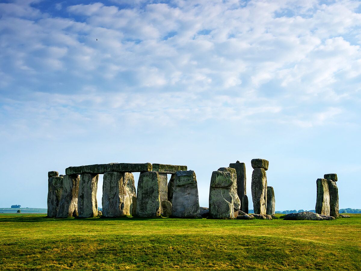 Stonehenge, prähistorisches Denkmal bei Wiltshire, England. Große aufrechte Steine und Querriegel in grüner Landschaft unter blauem Himmel.