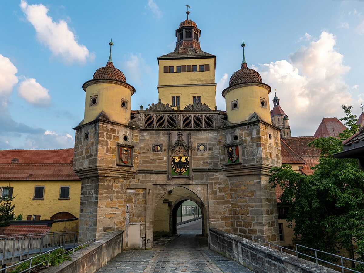 Imposantes mittelalterliches Stadttor aus Stein mit zwei Rundtürmen und einem hohen gelben Mittelturm unter blauem Himmel.