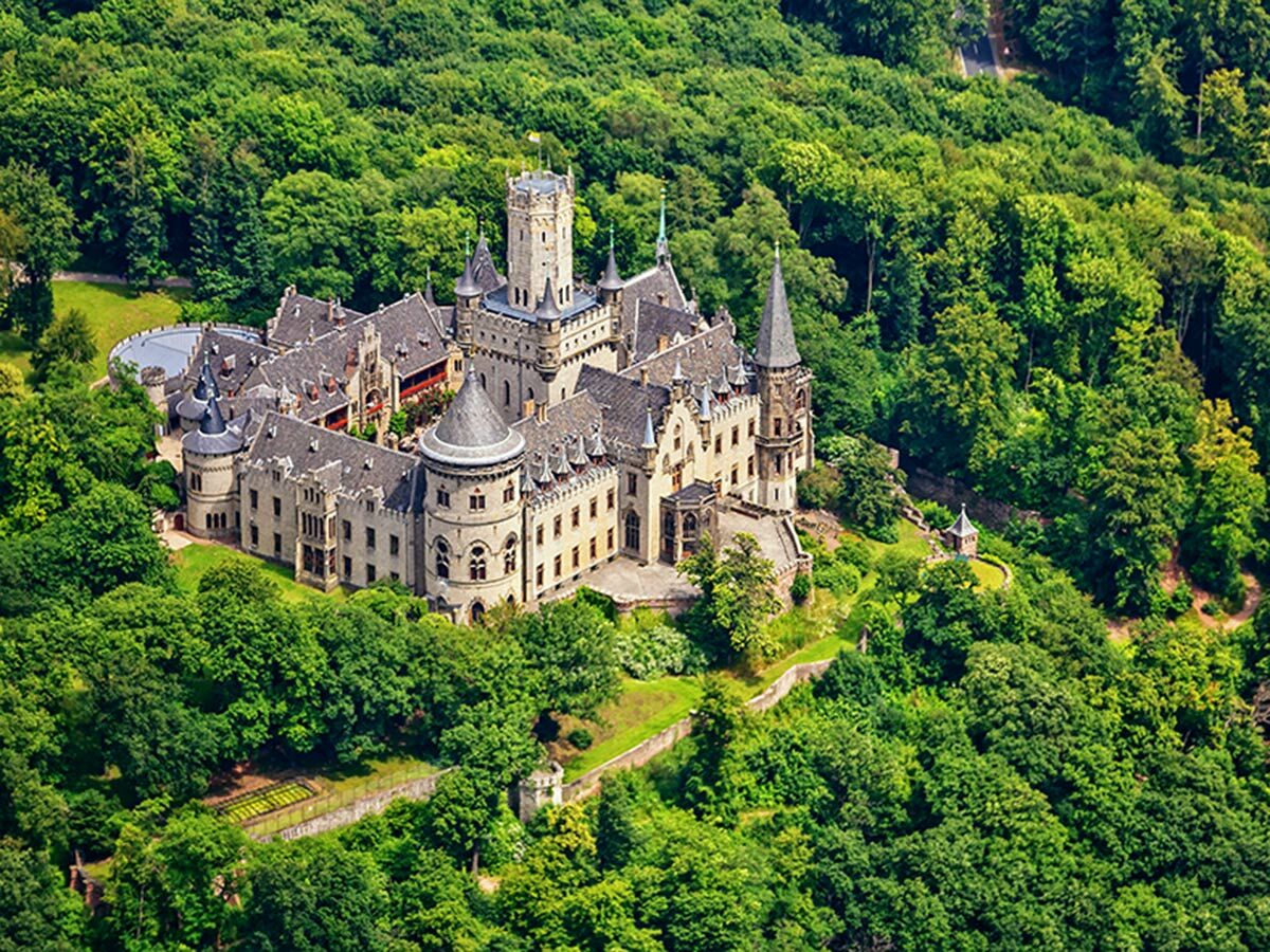 Luftaufnahme des Schlosses Marienburg in Deutschland, umgeben von dichtem, grünem Wald an einem sonnigen Tag.