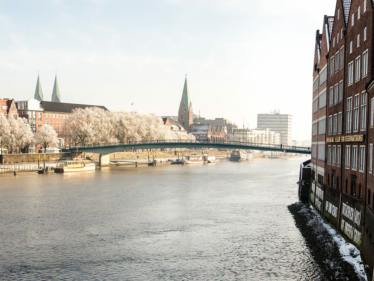 Winterliche Stadtansicht von Bremen mit Weserfluss, Brücke, historischen Gebäuden, Reifbäumen und moderner Architektur.