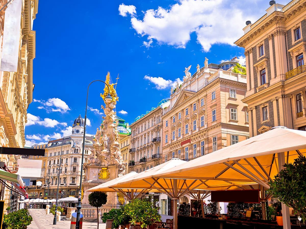 Blick auf den Graben in Wien mit der Pestsäule, eleganten Gebäuden, blauem Himmel und sonnigen Straßencafés.