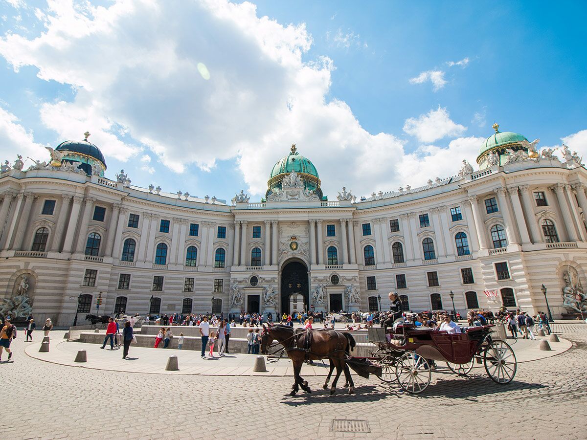 Historischer Michaelertrakt der Hofburg in Wien mit Pferdekutschen, Touristen und blauem Himmel.