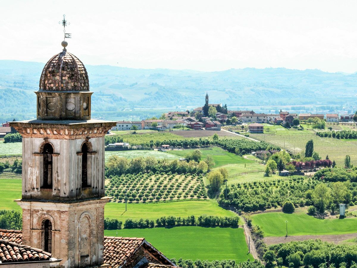 Historischer Kirchturm über grünen Weinbergen und einem Dorf in der malerischen italienischen Hügellandschaft.