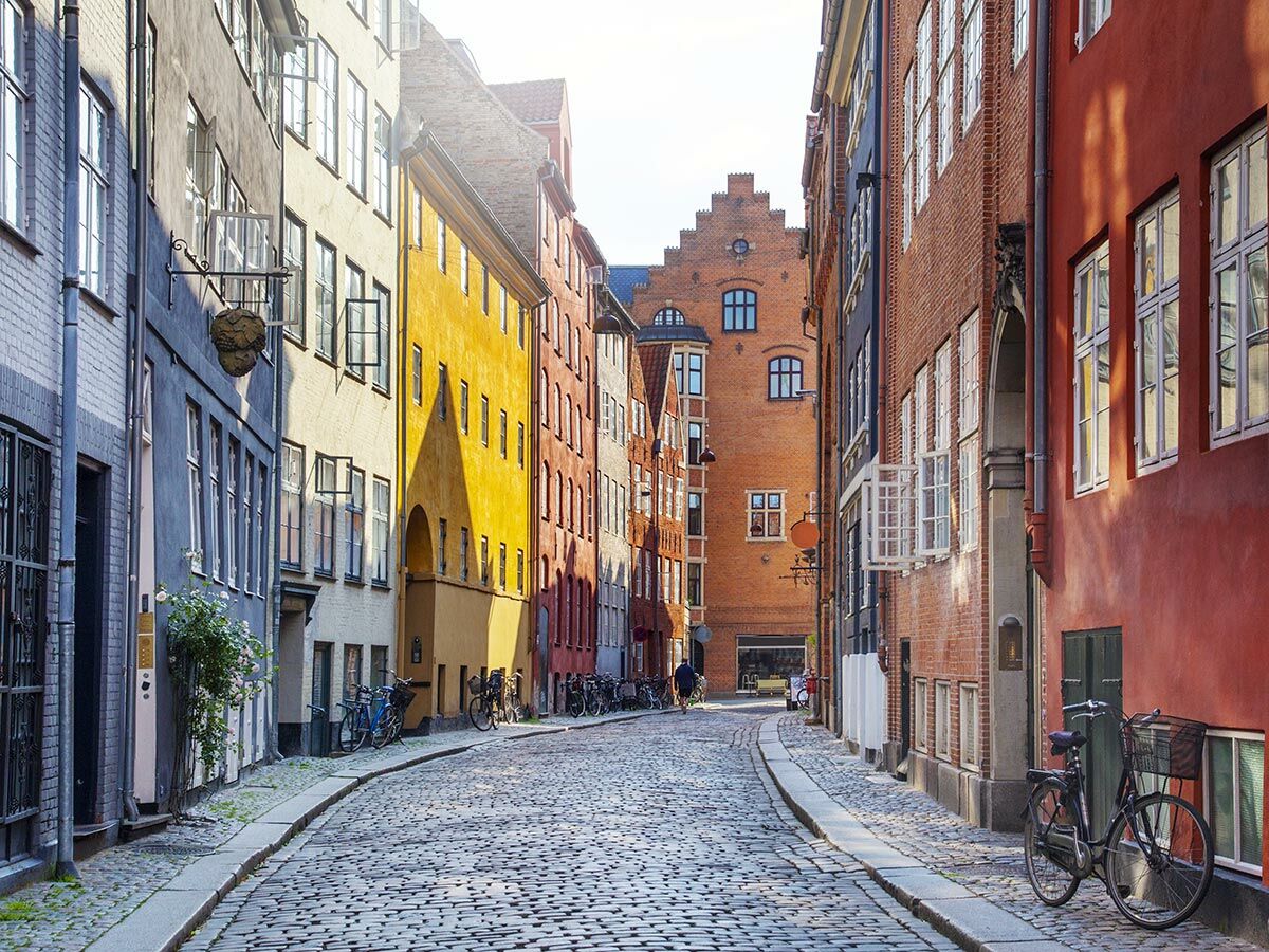 Kopfsteinpflastergasse in Kopenhagen mit farbenfrohen Altbauten, Fahrrädern und Sonnenlicht.