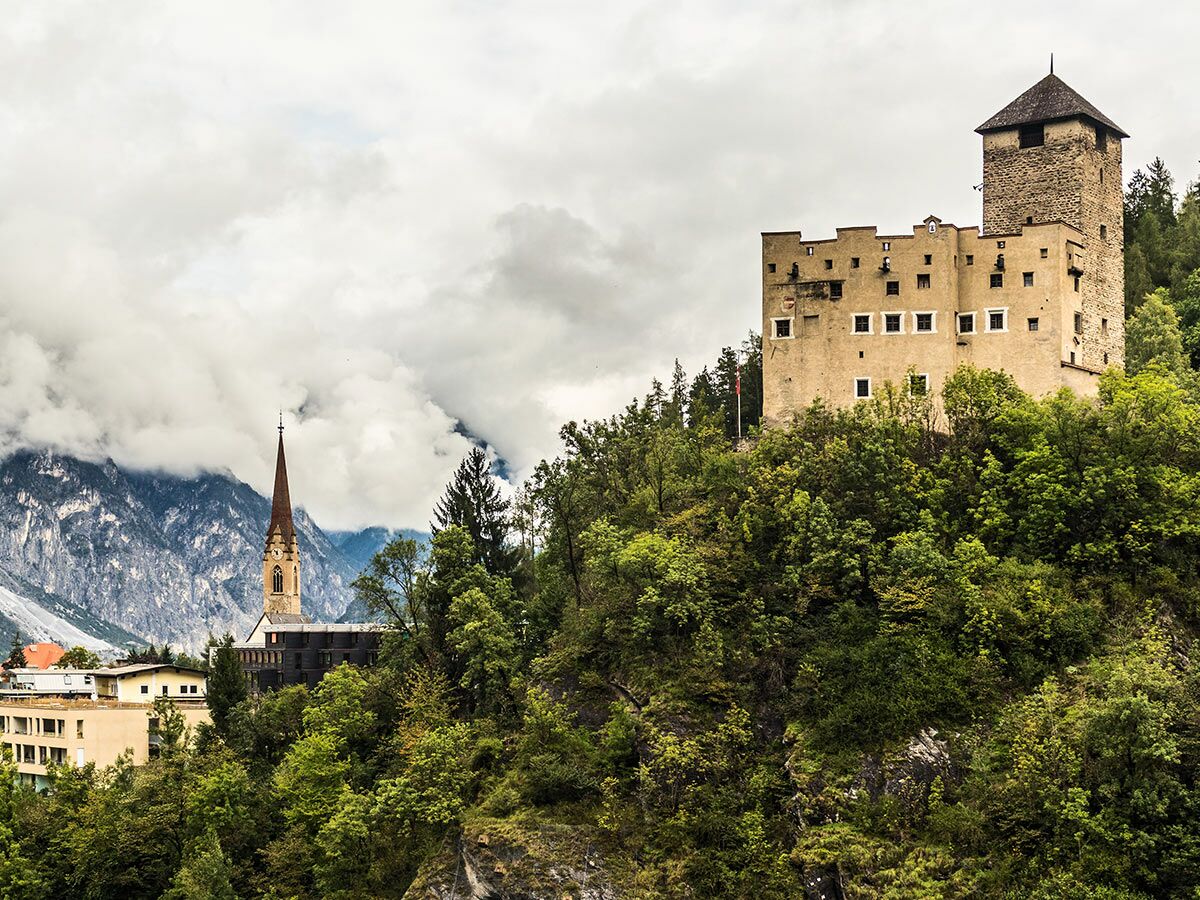 Panoramablick auf ein Schloss, eine Bergkirche und majestätische Alpenlandschaft mit Wolken in Südtirol.