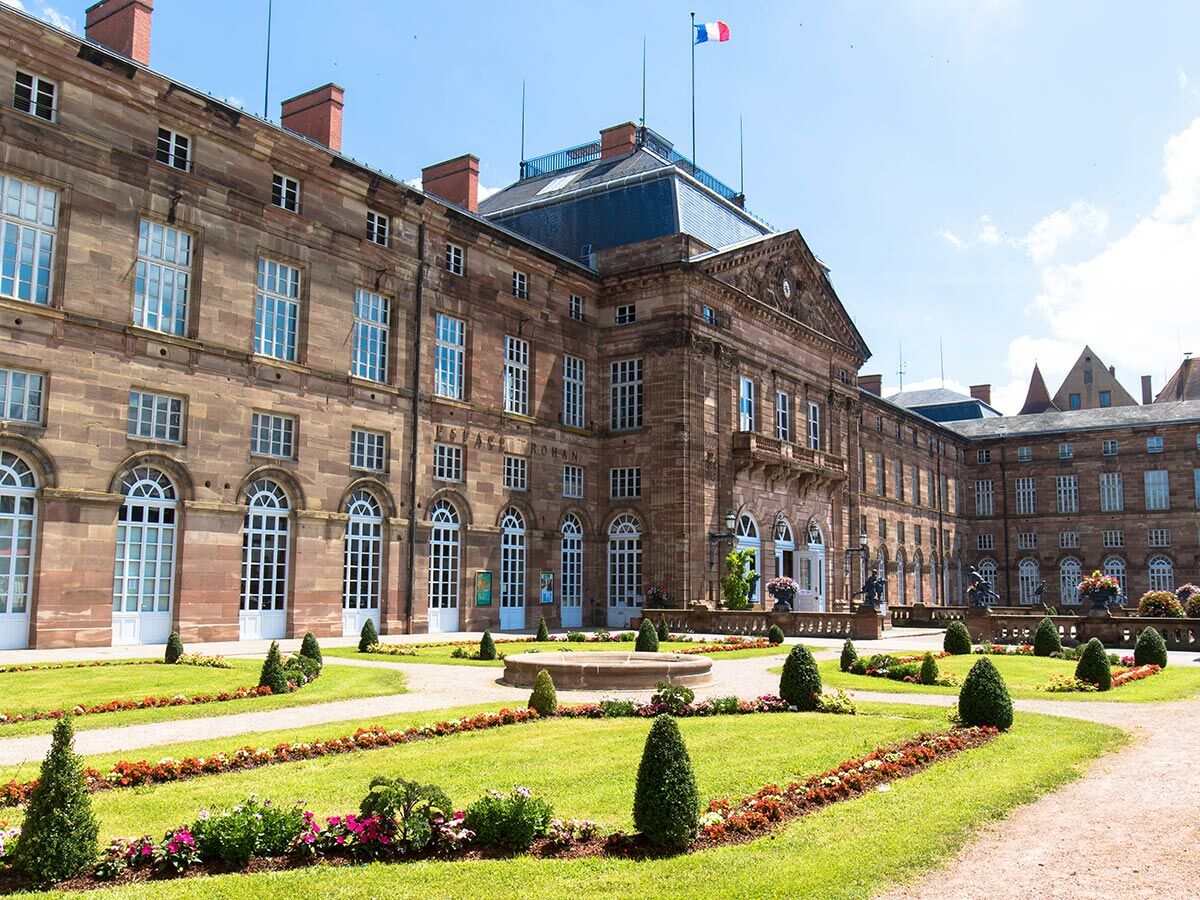 Das Palais Rohan in Straßburg an einem sonnigen Tag mit französischem Garten, rotem Sandstein und wehender Flagge.
