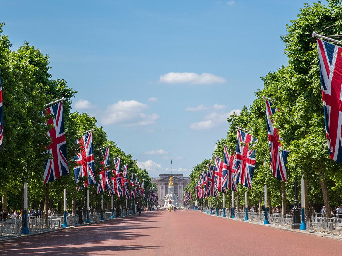 Blick auf Buckingham Palace entlang The Mall, gesäumt von vielen Union Jack Flaggen unter blauem Himmel in London.