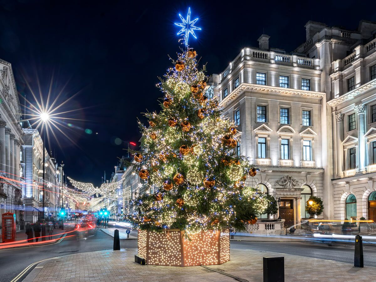 Großer, festlich beleuchteter Weihnachtsbaum in der Londoner Regent Street bei Nacht mit Engelflügel-Dekorationen und Lichtspuren von Fahrzeugen.