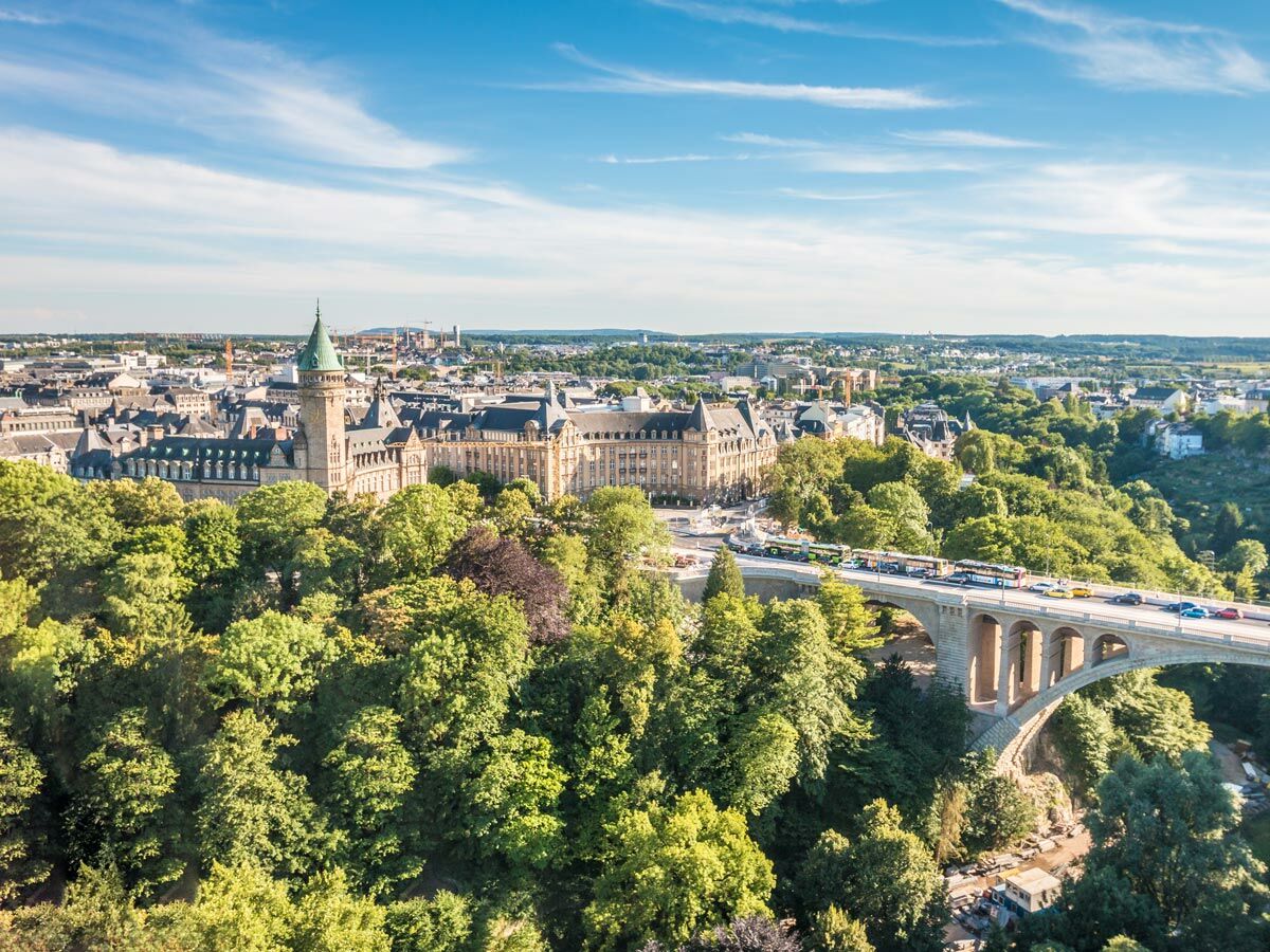 Luftbild Luxemburg Stadt mit Adolphe Brücke über grünes Tal, umgeben von historischen Gebäuden und markantem Turm.