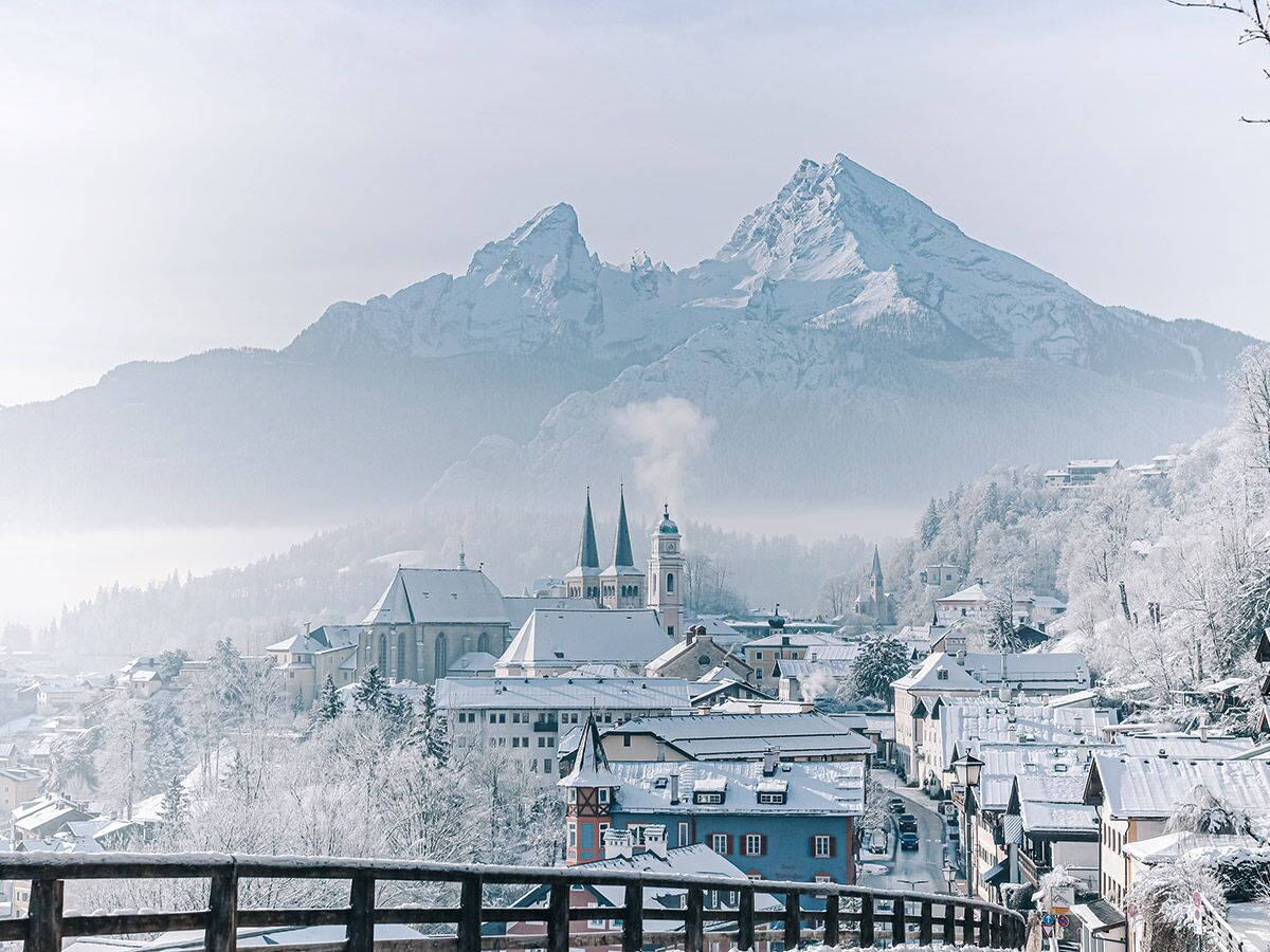 Verschneite Alpenstadt Berchtesgaden mit historischen Kirchen und majestätischen Watzmann-Bergen im Winter bei blauem Himmel.