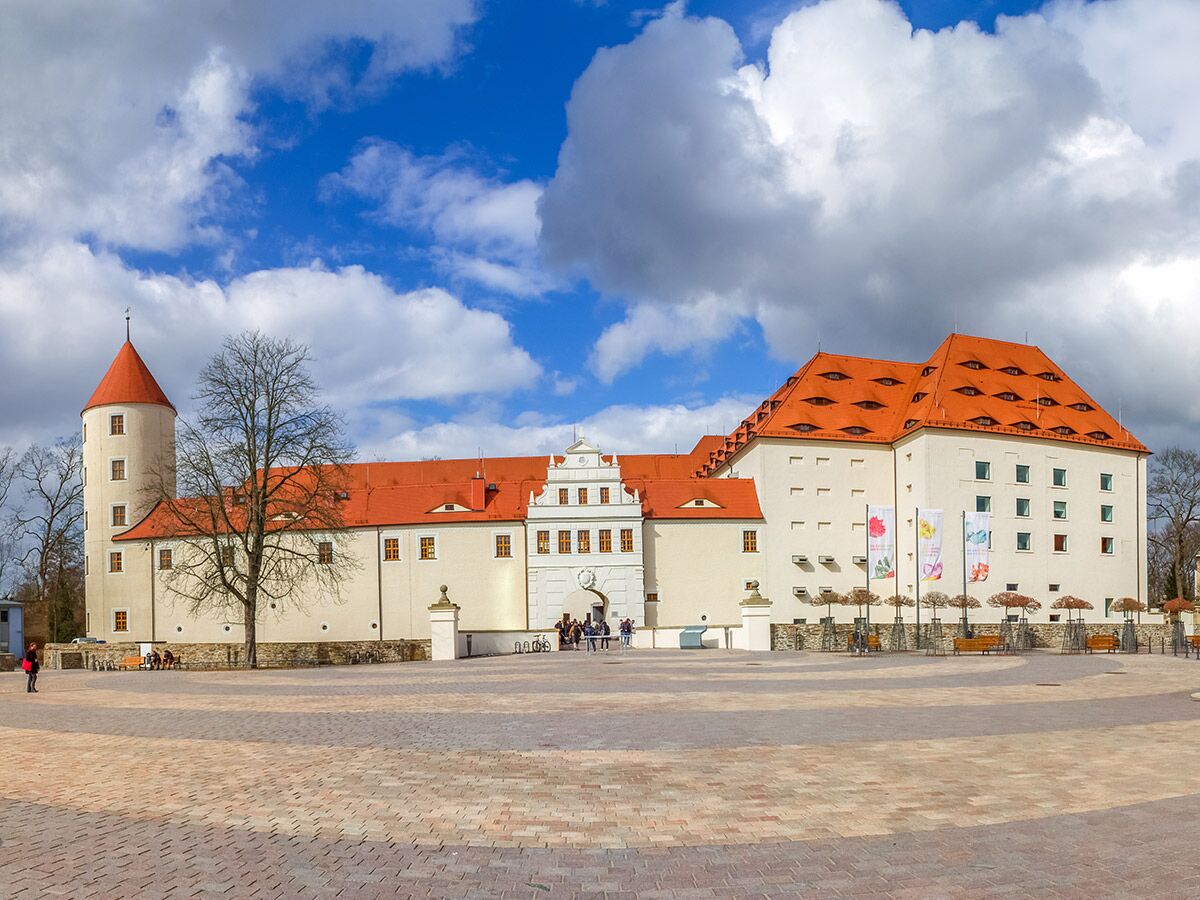 Schloss Hartenfels in Torgau mit rundem Turm, markanten roten Dächern, großem Vorplatz und Menschen an einem sonnigen Tag.