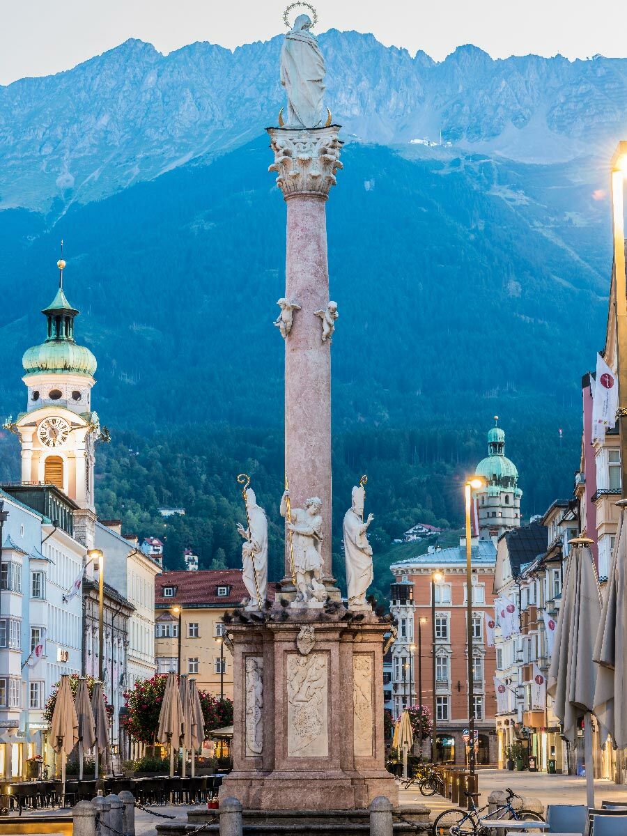 Historische Annasäule in Innsbruck mit Marienstatue, umgeben von Altstadtgebäuden und den majestätischen Alpen.