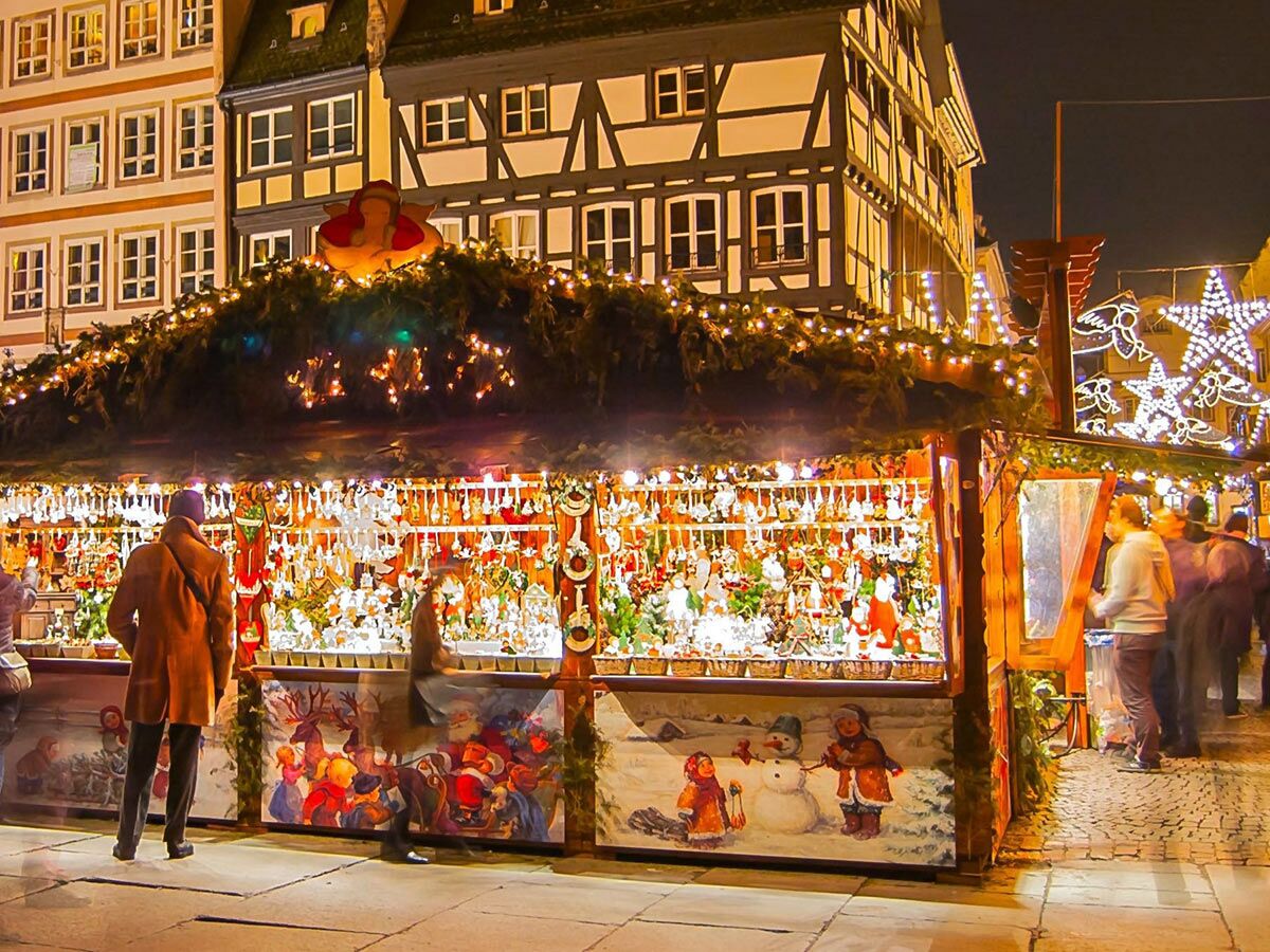 Beleuchteter Weihnachtsmarkt Stand mit festlichen Dekorationen und zahlreichen Ornamenten. Besucher stöbern zwischen den Waren bei Nacht.