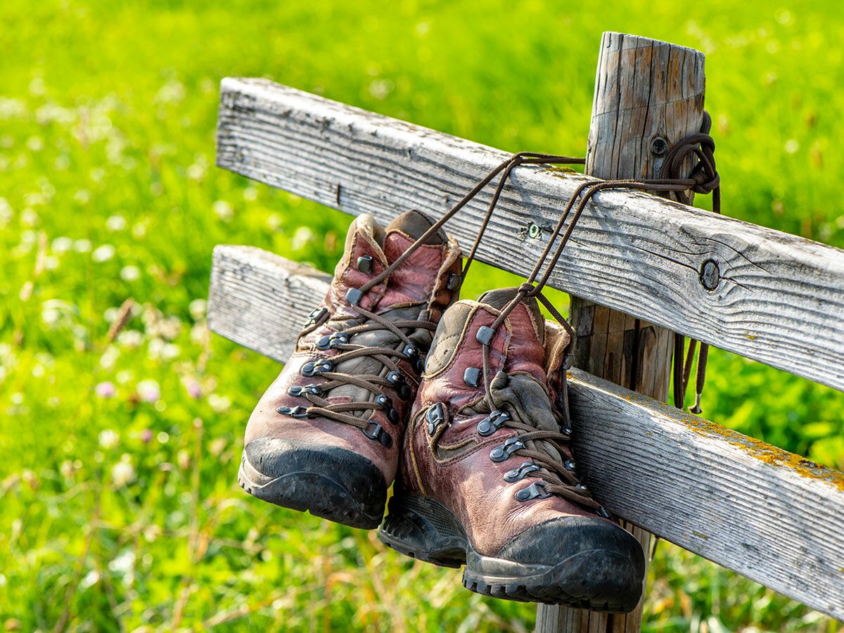 Ein Paar braune Wanderstiefel hängt über einen rustikalen Holzzaun vor einer unscharfen grünen Wiese.