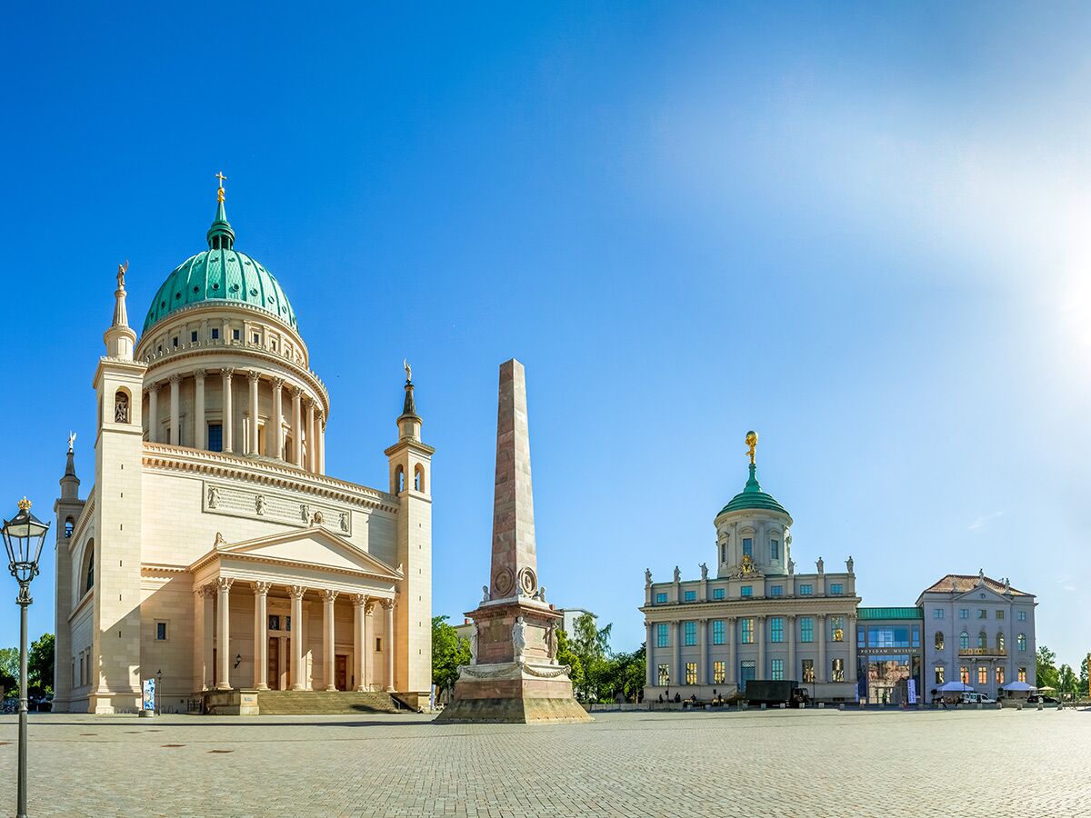 Panoramablick auf den Alten Markt in Potsdam mit der St. Nikolaikirche, dem Obelisken und dem Alten Rathaus bei blauem Himmel.