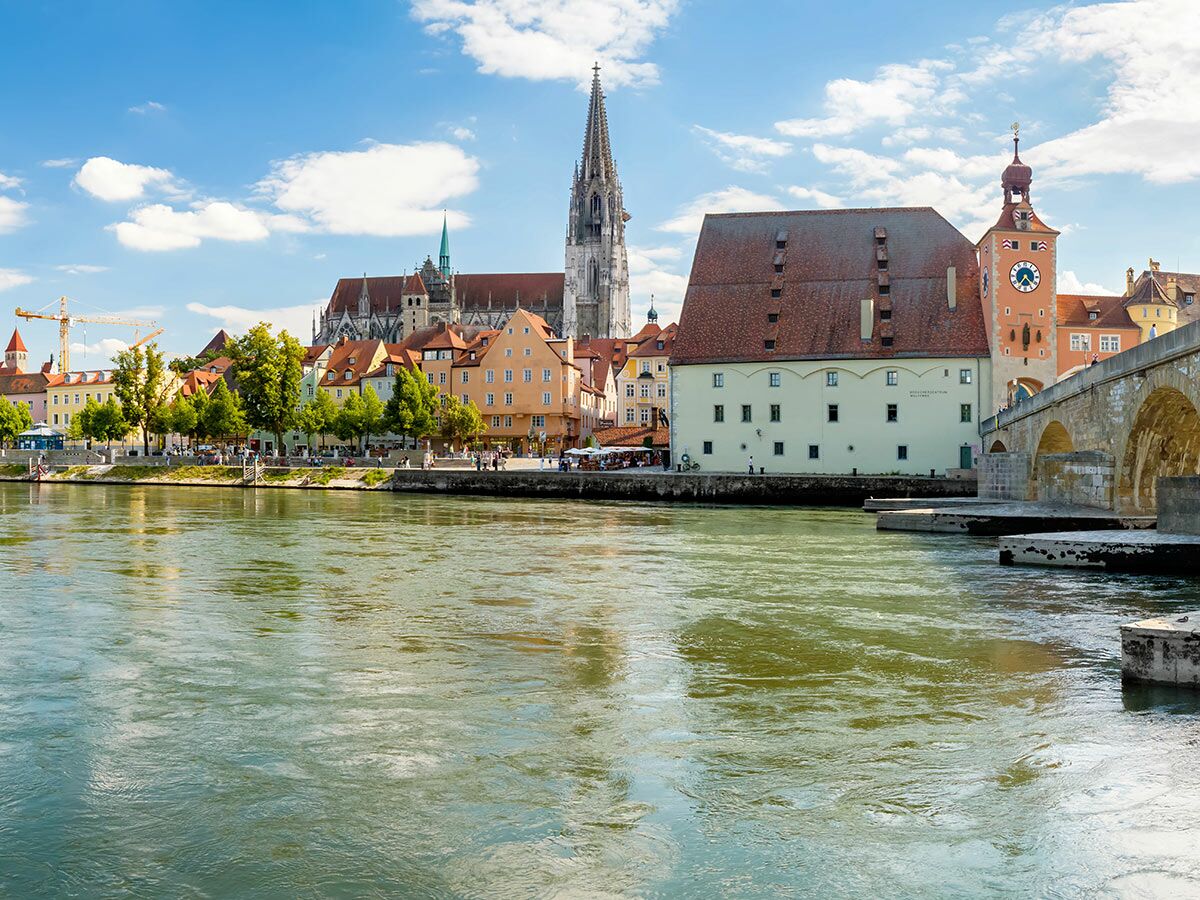 Panorama von Regensburg mit Steinerner Brücke, Dom und Altstadt am Ufer der Donau unter blauem Himmel.