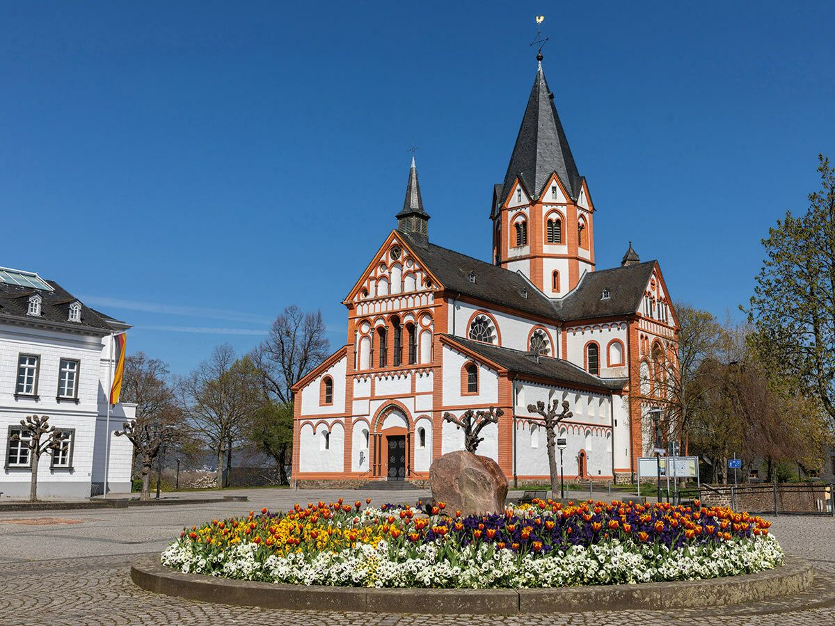 Die romanische Basilika St. Kastor in Koblenz mit farbenfrohem Blumenbeet vor strahlend blauem Himmel an einem sonnigen Frühlingstag.