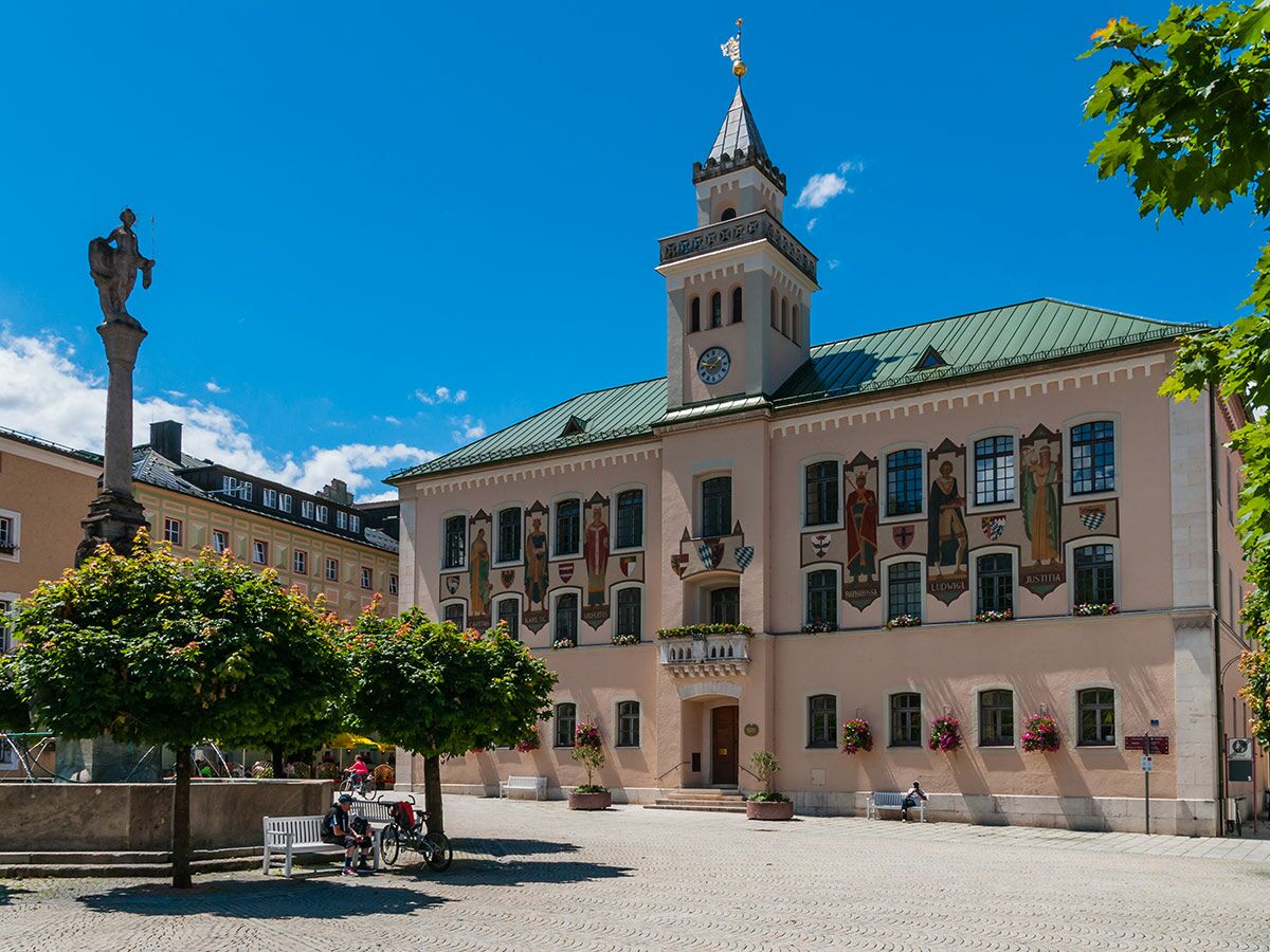 Historisches Rathaus am Marktplatz mit Uhr, Turm, kunstvollen Fassadenmalereien und einer Statue unter blauem Himmel in einer europäischen Stadt.