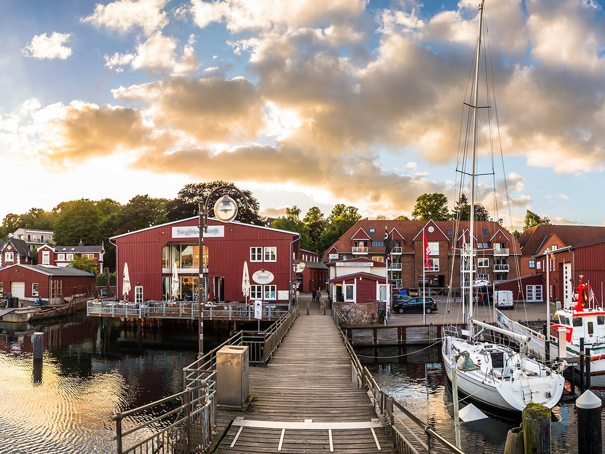 Malerischer Hafen bei Sonnenuntergang mit roten Gebäuden, Holzsteg und Segelbooten. Idylle in einer norddeutschen Marina.