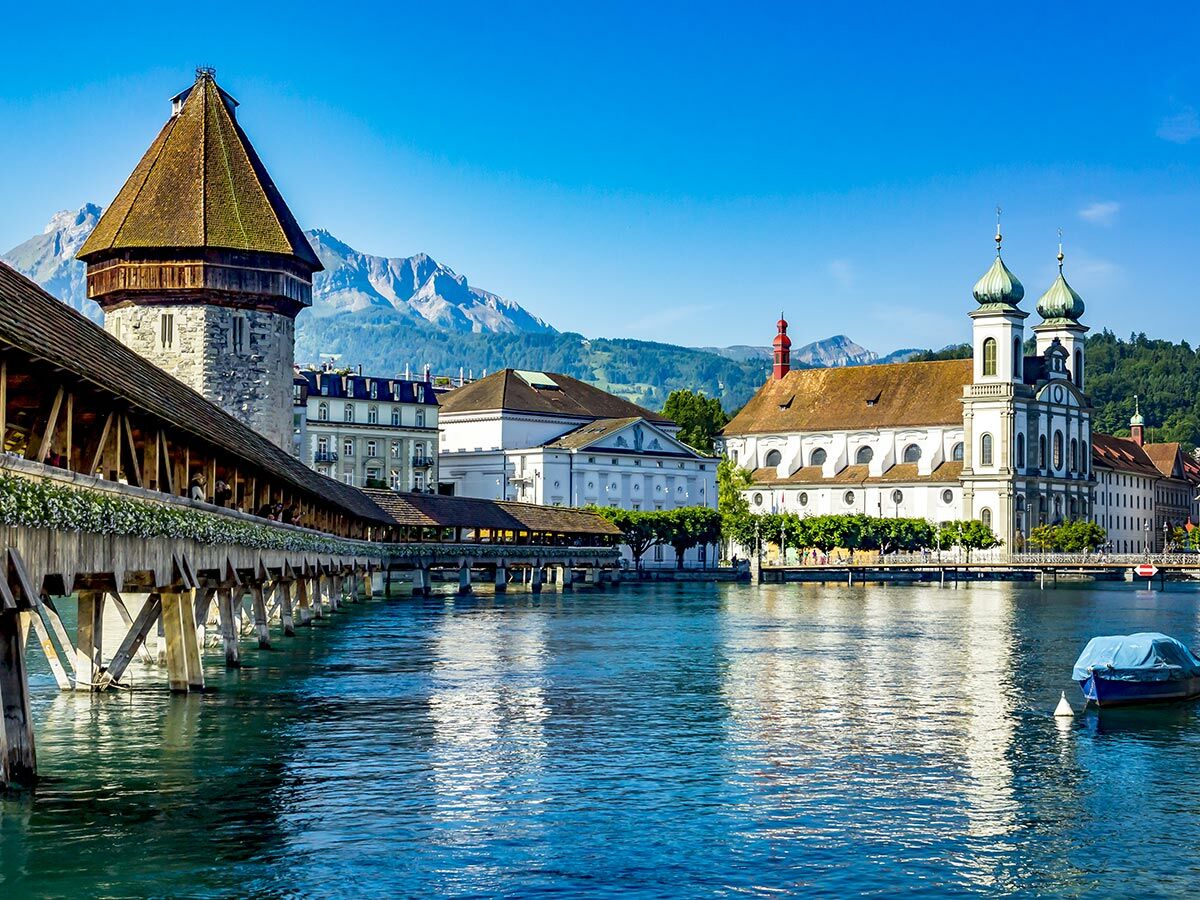 Historische Kapellbrücke mit Wasserturm und Jesuitenkirche am Fluss Reuss in Luzern, Schweiz, vor Alpenkulisse.