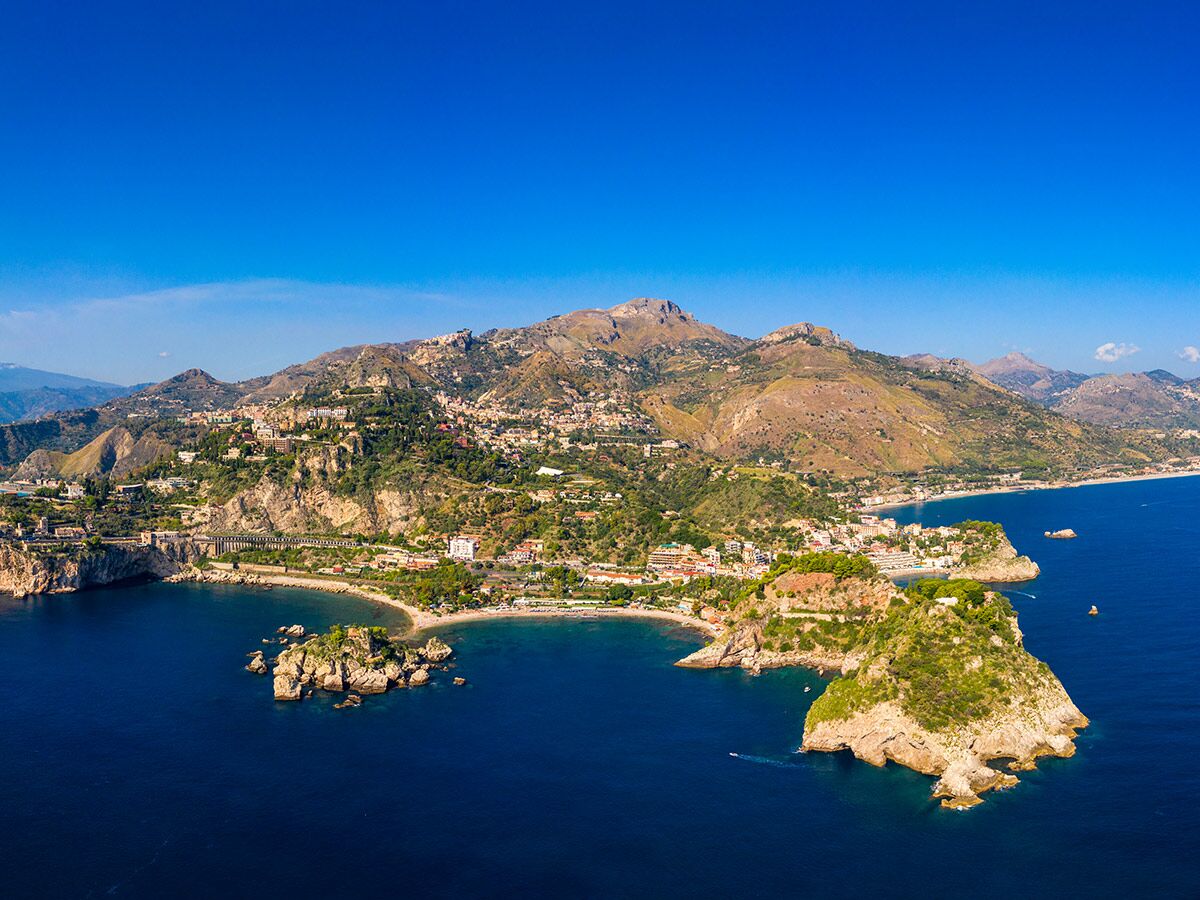 Luftbild von Taormina in Sizilien mit der Isola Bella, Küste, Stränden und Bergen unter blauem Himmel.