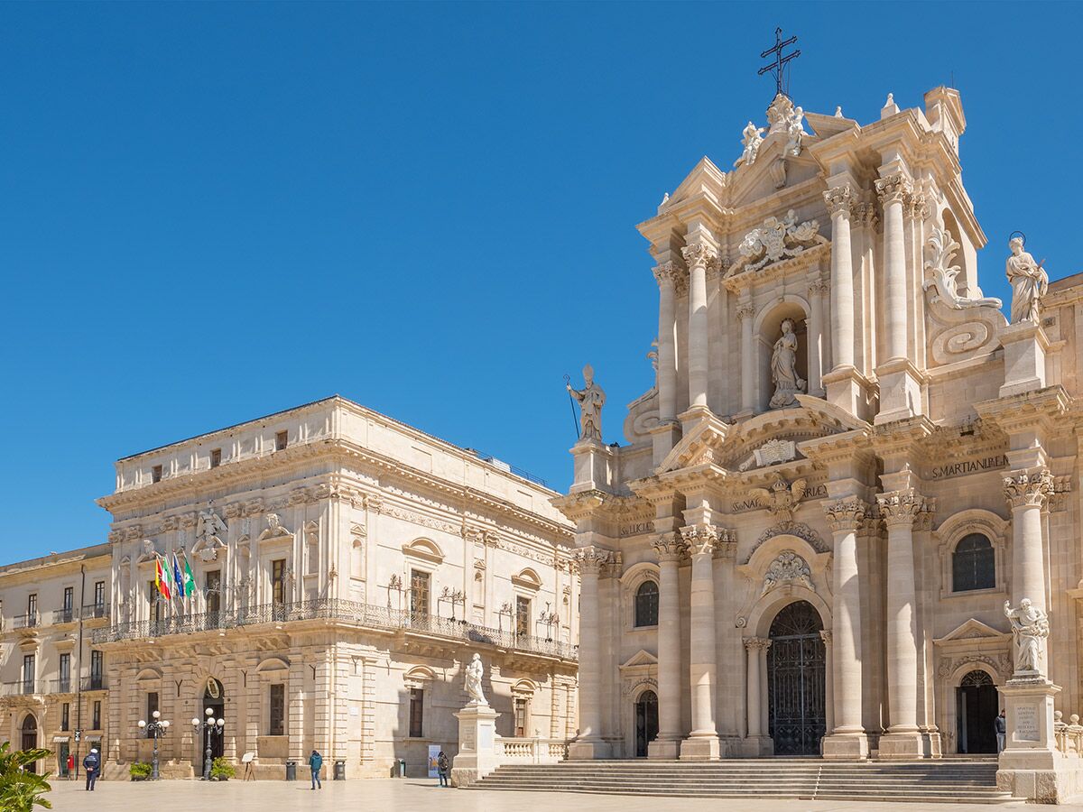 Barocke Kathedrale von Syrakus am sonnigen Domplatz mit detailreicher Fassade und historischem Palazzo in Sizilien.