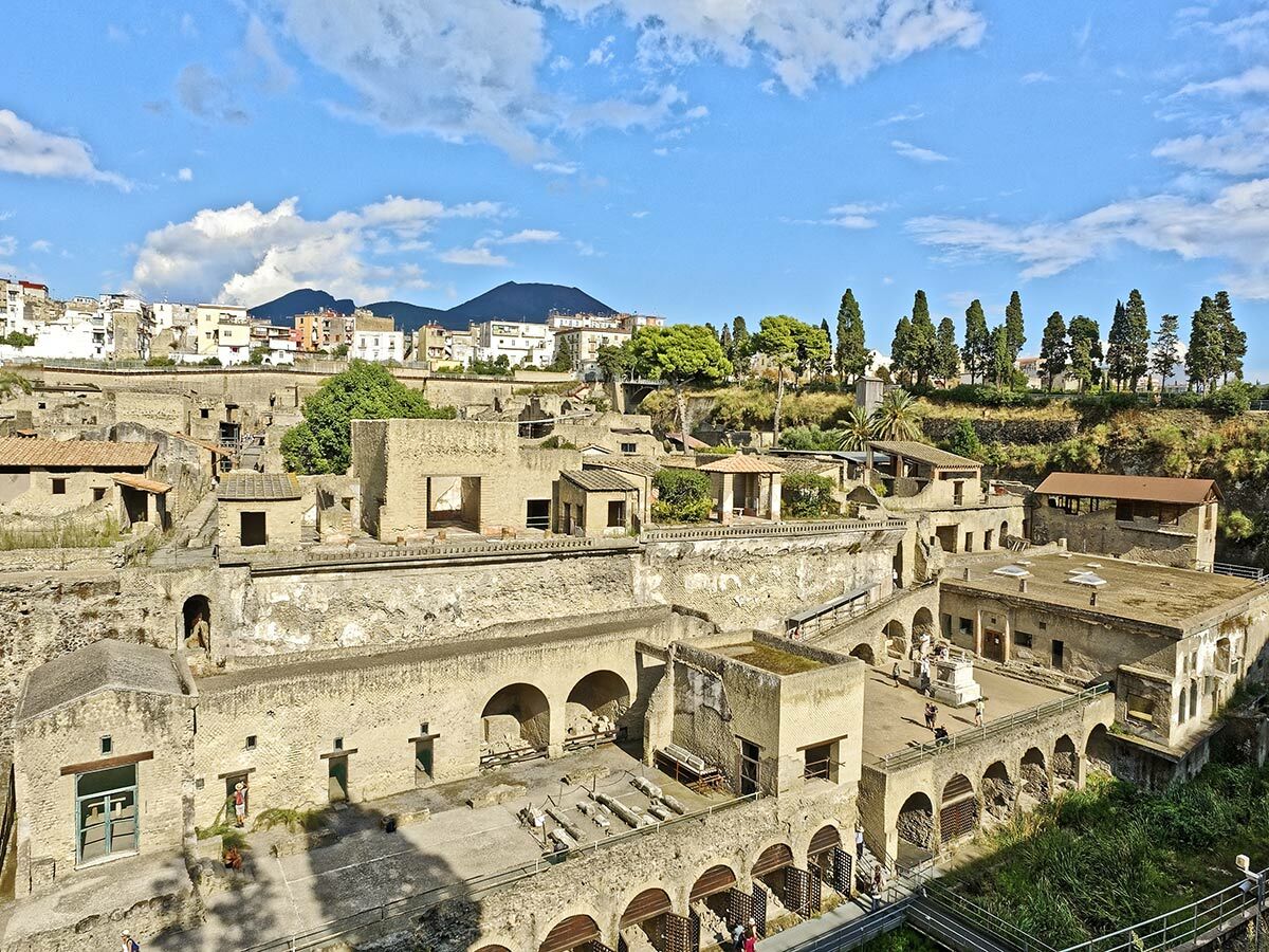 Luftaufnahme der antiken Stadt Herculaneum mit gut erhaltenen römischen Ruinen, Vesuv im Hintergrund und Touristen.