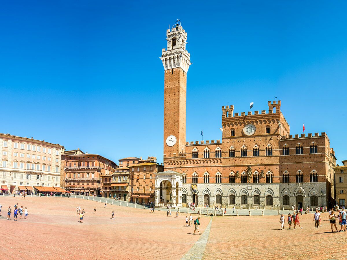Blick auf die Piazza del Campo in Siena mit dem Palazzo Pubblico, dem Torre del Mangia und Menschen an einem sonnigen Tag.
