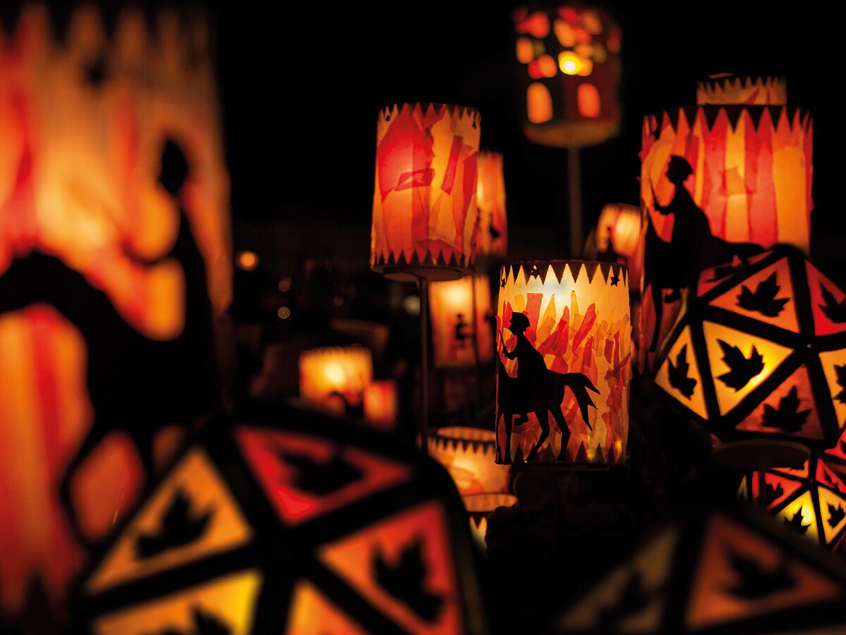 Nahaufnahme festlicher, beleuchteter Laternen mit Scherenschnitten von Reitern auf Pferden und Ahornblättern in warmen Herbstfarben.