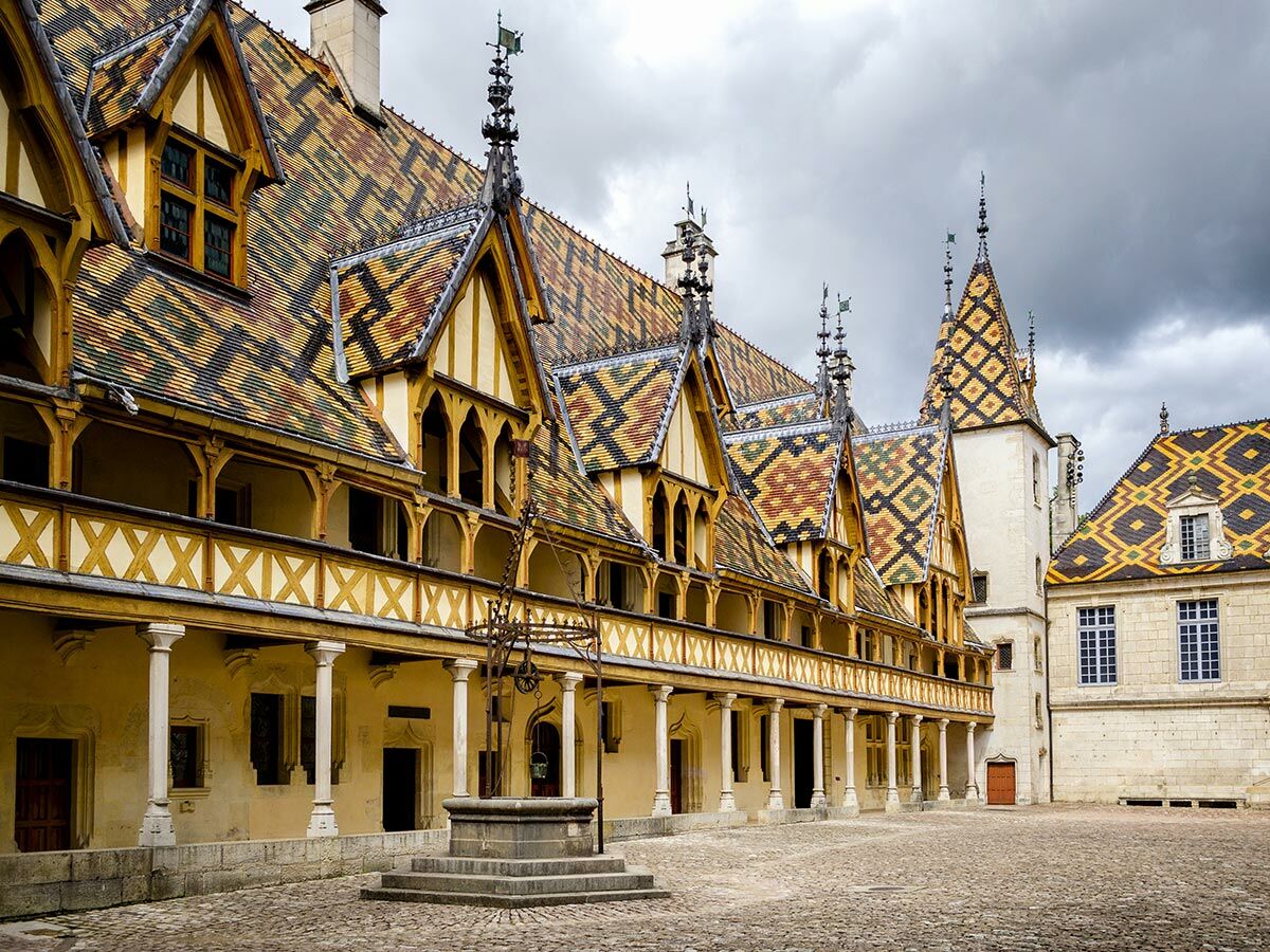 Hospices de Beaune Innenhof mit seinen ikonischen bunten Ziegeldächern, Säulenarkaden und einem Brunnen in Burgund, Frankreich.