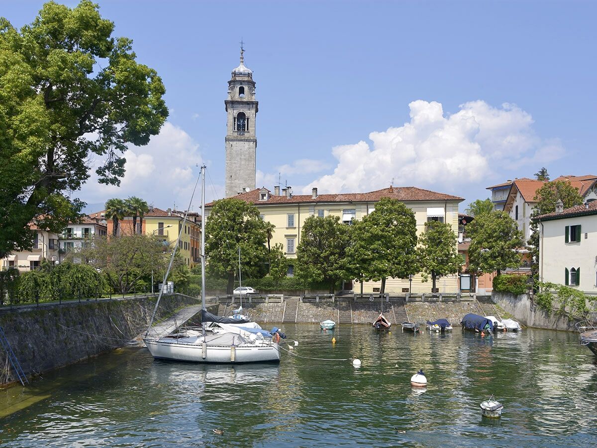 Malerische italienische Seestadt mit Glockenturm, bunten Häusern und Booten am Wasser unter blauem Himmel mit Wolken.
