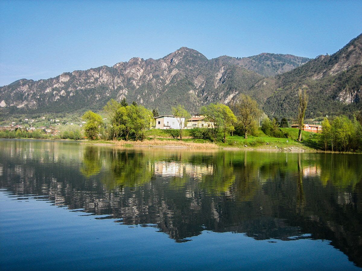 Ein ruhiger Bergsee spiegelt grüne Bäume, Häuser und majestätische Alpen im Sonnenlicht wider. Idylle in der Natur.